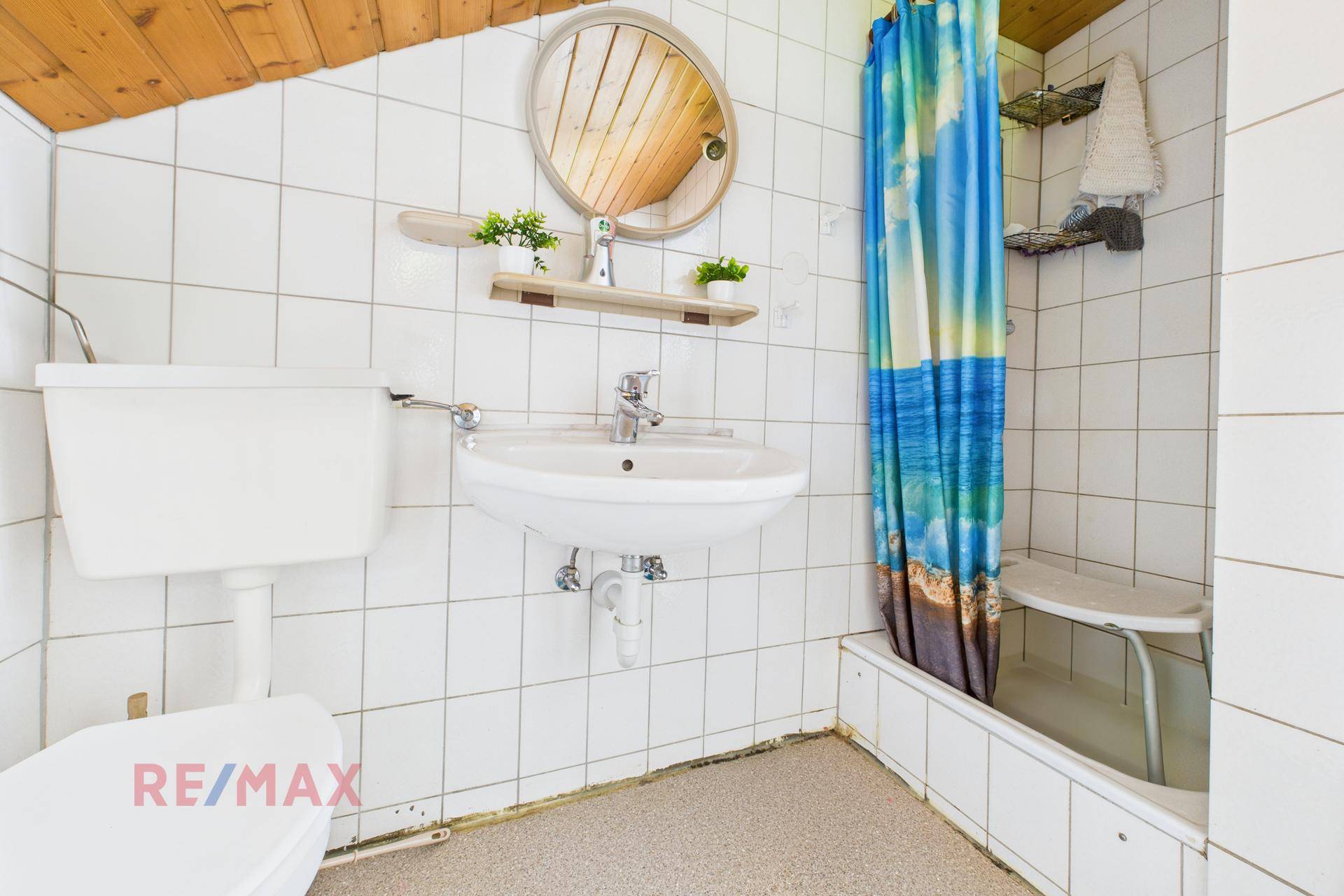 Badezimmer mit Dusche, WC und Waschbecken, ausgestattet mit weißen Fliesen und Dachschräge.