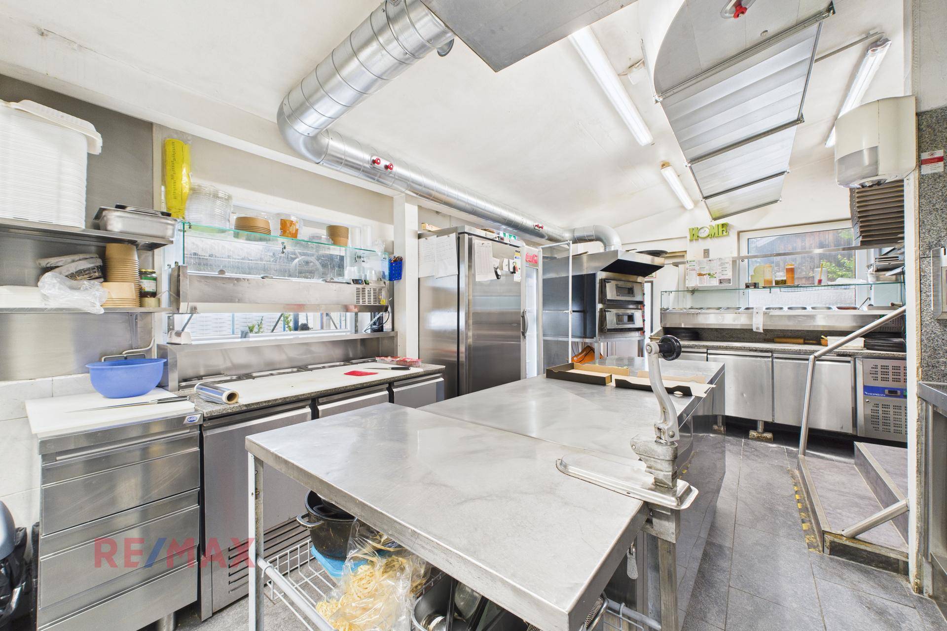 Geräumige professionelle Küche mit mehreren Arbeitsbereichen, großen Kühlgeräten und Fenster.