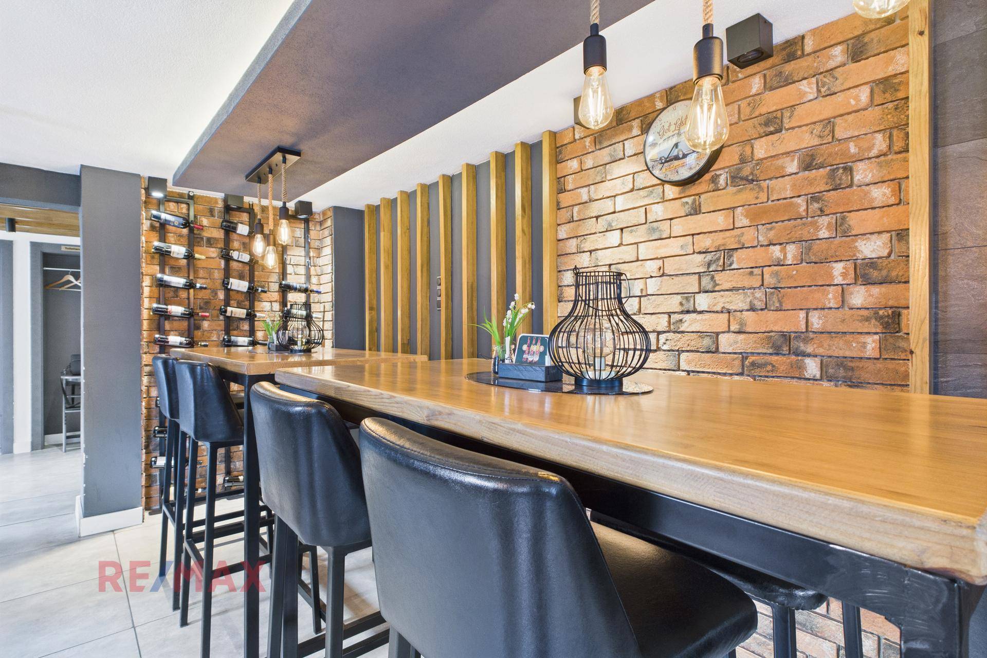 Detailansicht der Bartheke mit Holzplatte, hohen Hockern und Weinflaschenregal an der Ziegelwand.