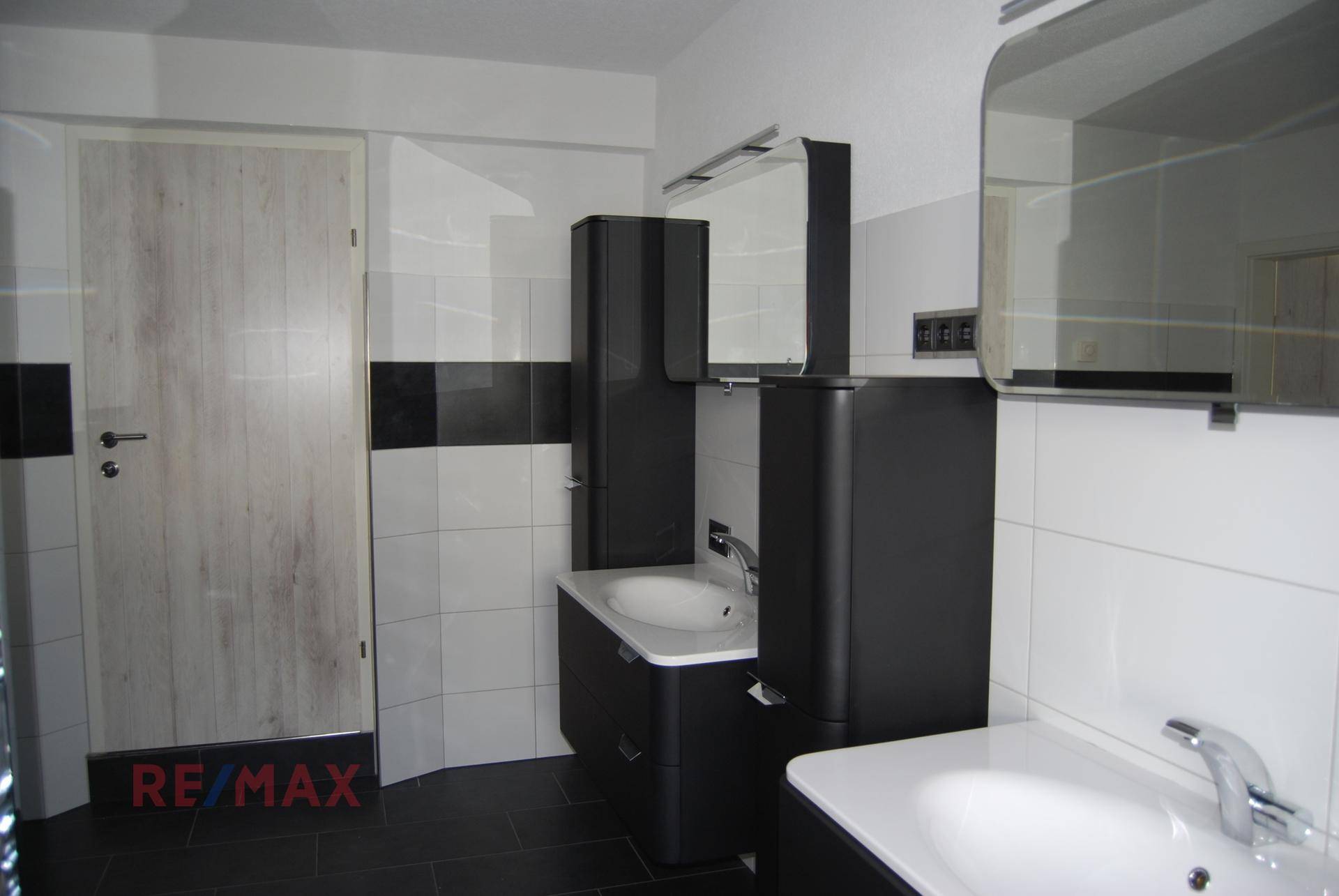 Badezimmer mit zwei Waschbecken, schwarzen Badmöbeln und weißen Wandfliesen.