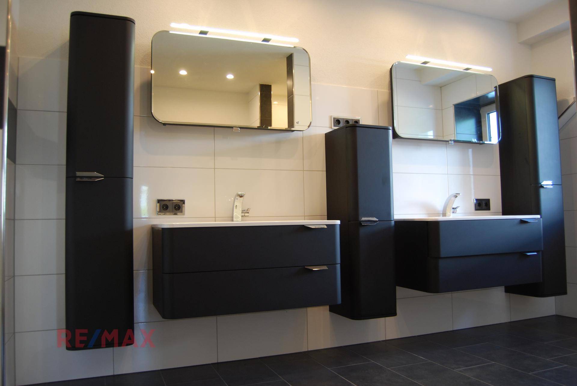 Modernes Badezimmer mit Doppelwaschbecken, schwarzen Schränken und Spiegelschränken.