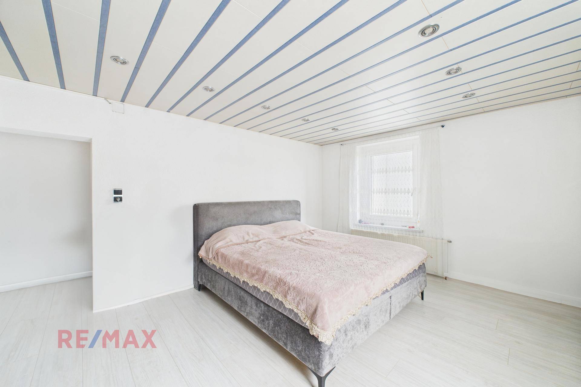Helles Schlafzimmer mit Doppelbett, weiß gestrichenen Wänden und Laminatboden.
