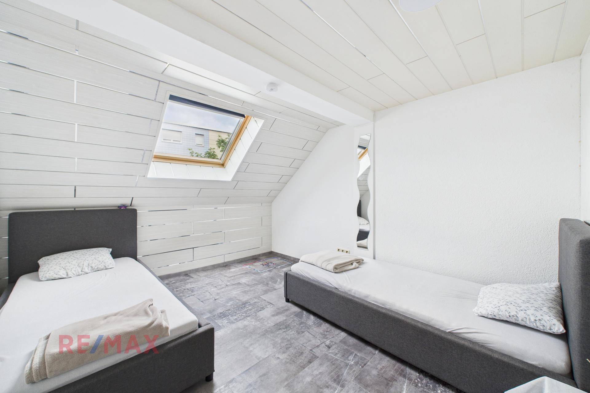 Dachschlafzimmer mit zwei Einzelbetten, Schrägdach und Dachfenster für Tageslicht.