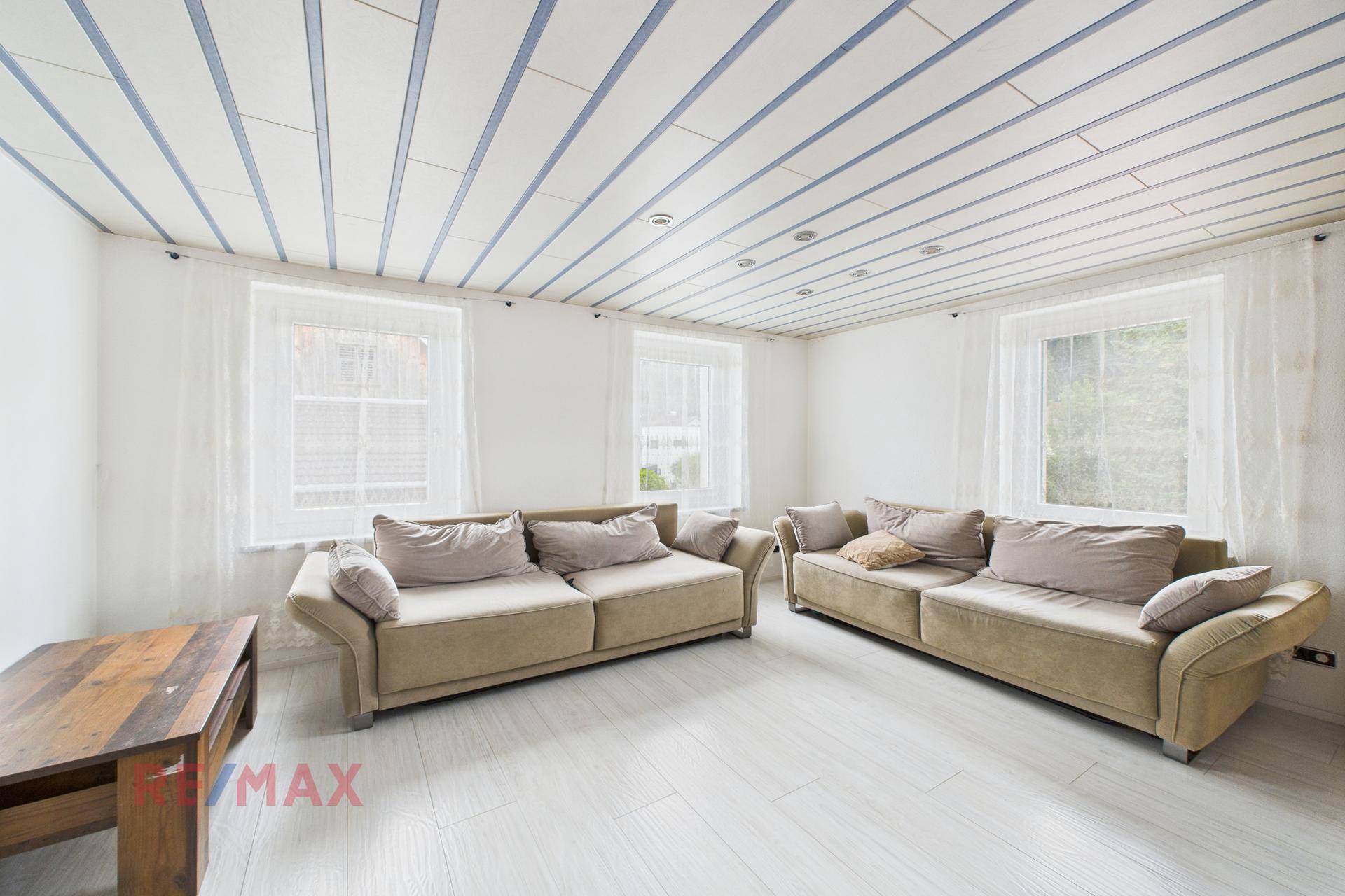Geräumiges Wohnzimmer mit zwei Sofas, hellem Boden und gestreifter Holzdecke.