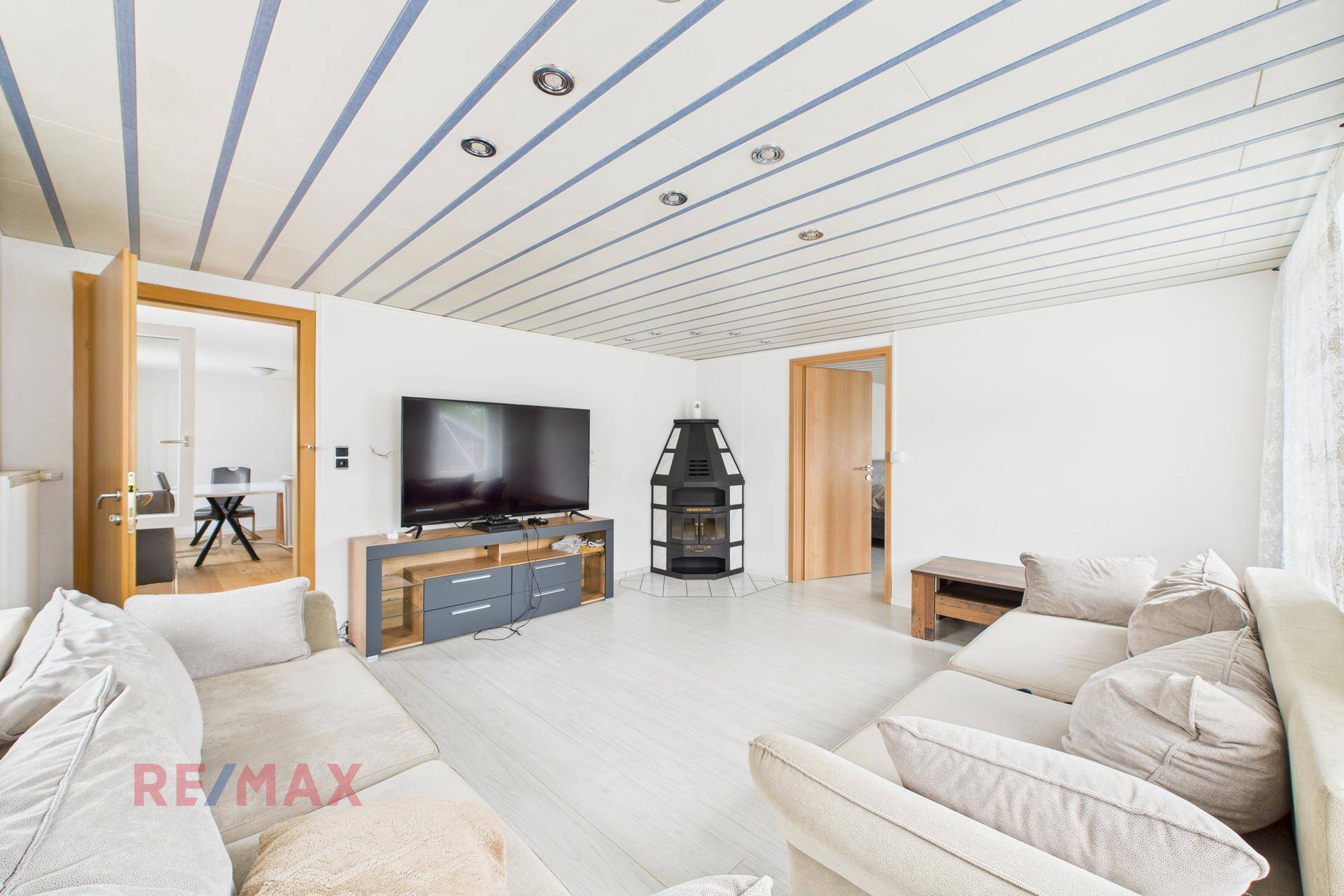 Gemütliches Wohnzimmer mit Kaminofen, großem Fernseher und bequemen Sofas.