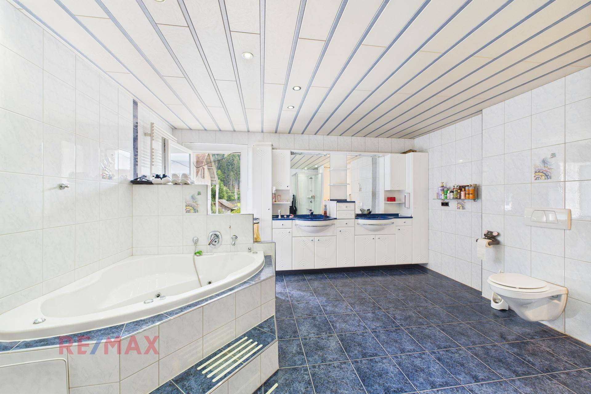 Großes Badezimmer mit Eckbadewanne, Doppelwaschbecken und blauen Bodenfliesen.
