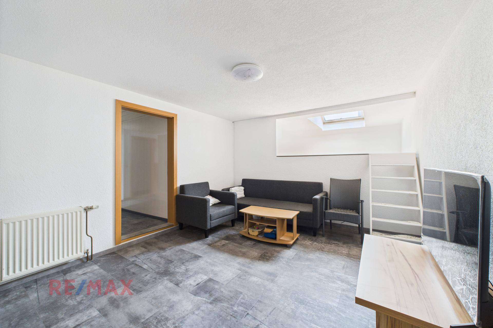 Gemütlicher Wohnbereich im Untergeschoss mit Sofa, Sessel und Dachfenster.
