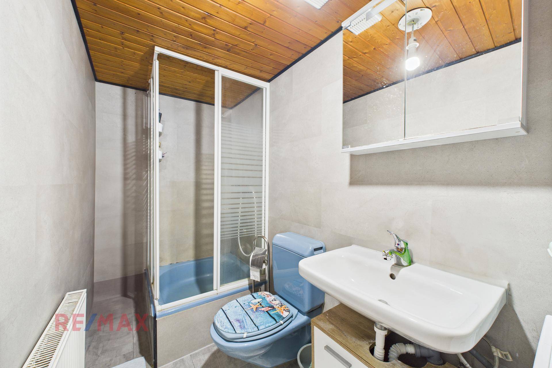 Kleines Badezimmer mit Duschkabine, Waschbecken und blauer Toilette.