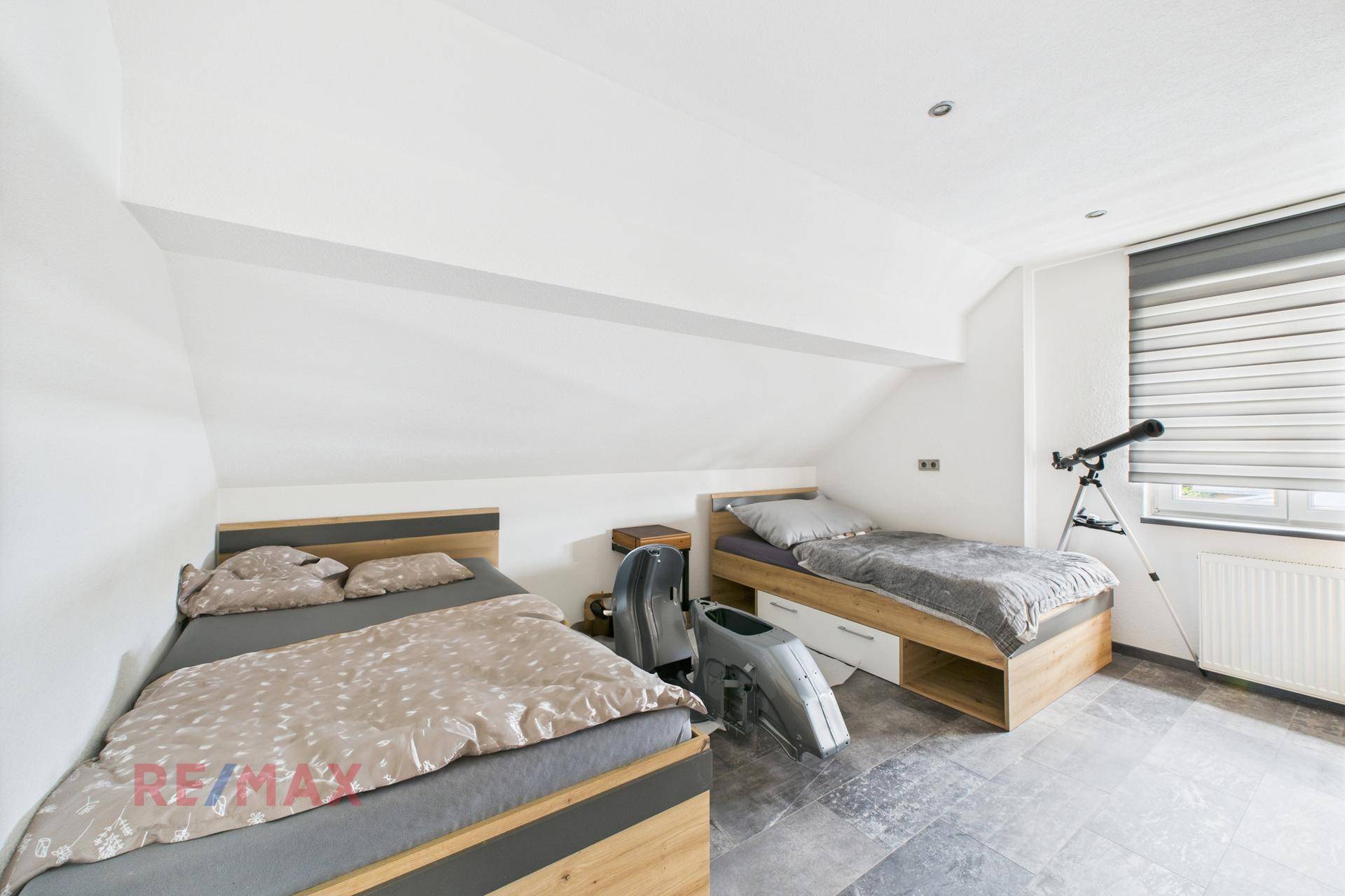 Schlafzimmer mit zwei Einzelbetten, Schrägdach und Fenster mit Jalousie.