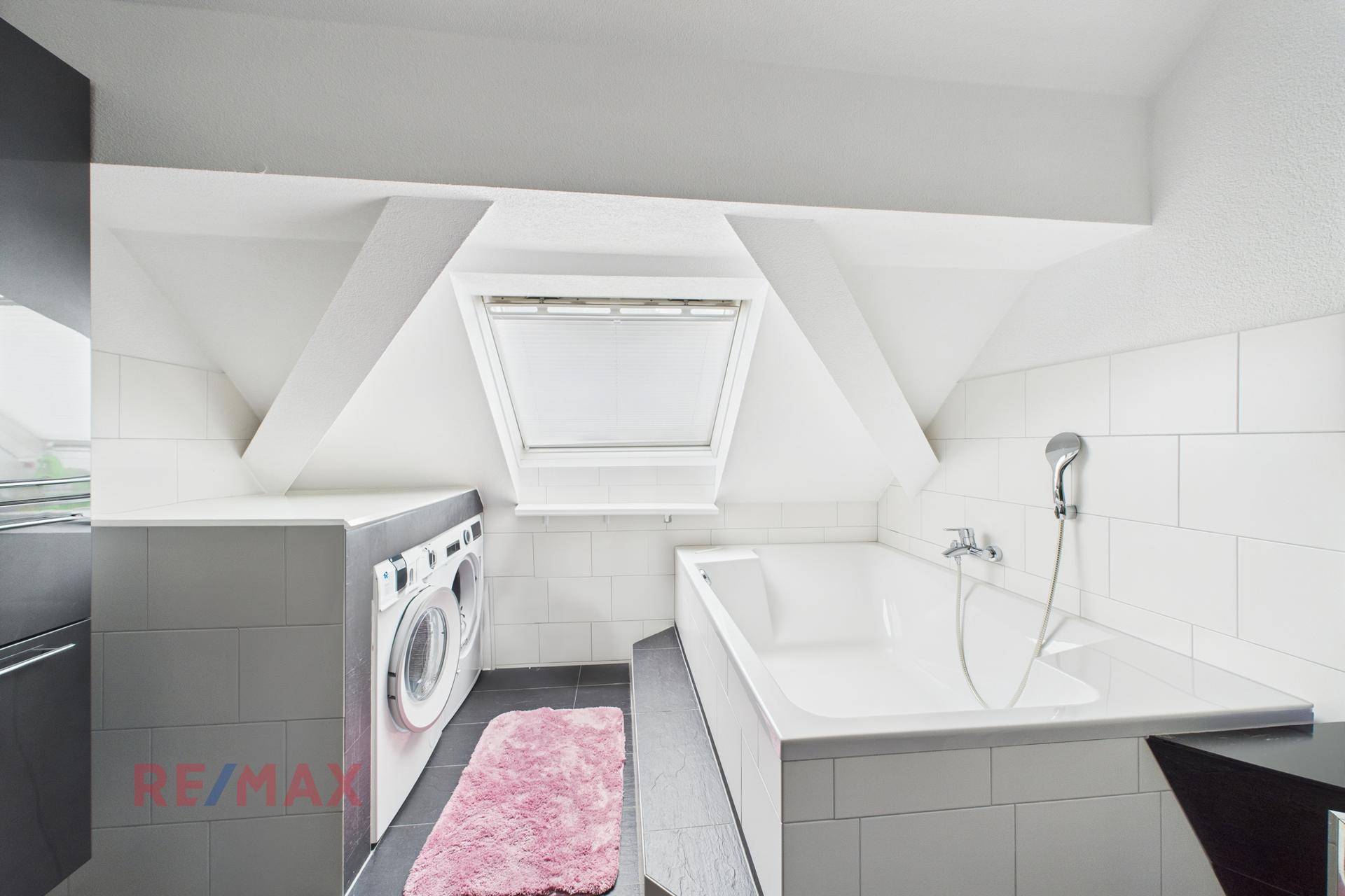 Badezimmer im Dachgeschoss mit Badewanne, Waschmaschine und Dachfenster.