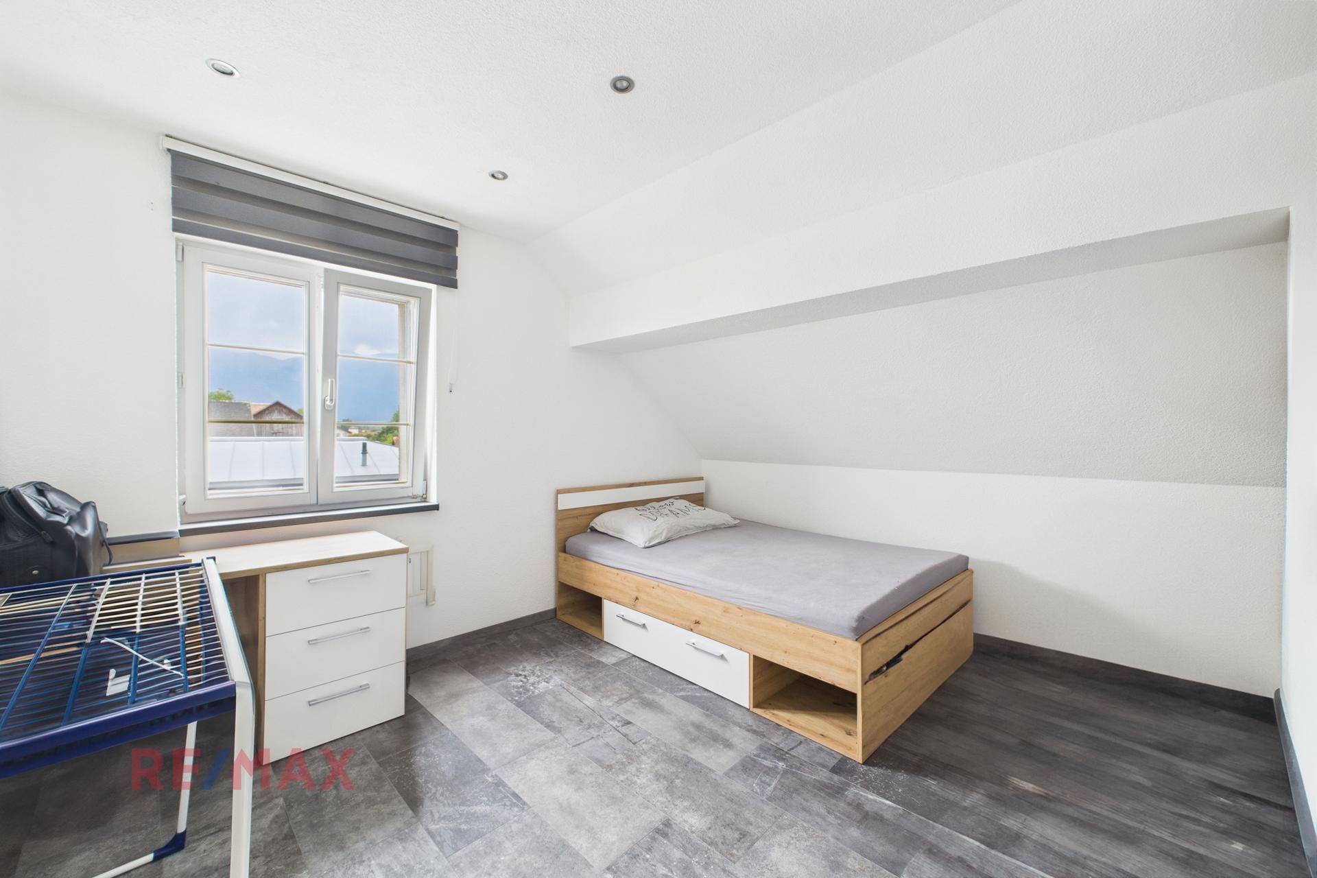 Helles Schlafzimmer mit Einzelbett, Schreibtisch und Fenster mit Ausblick.