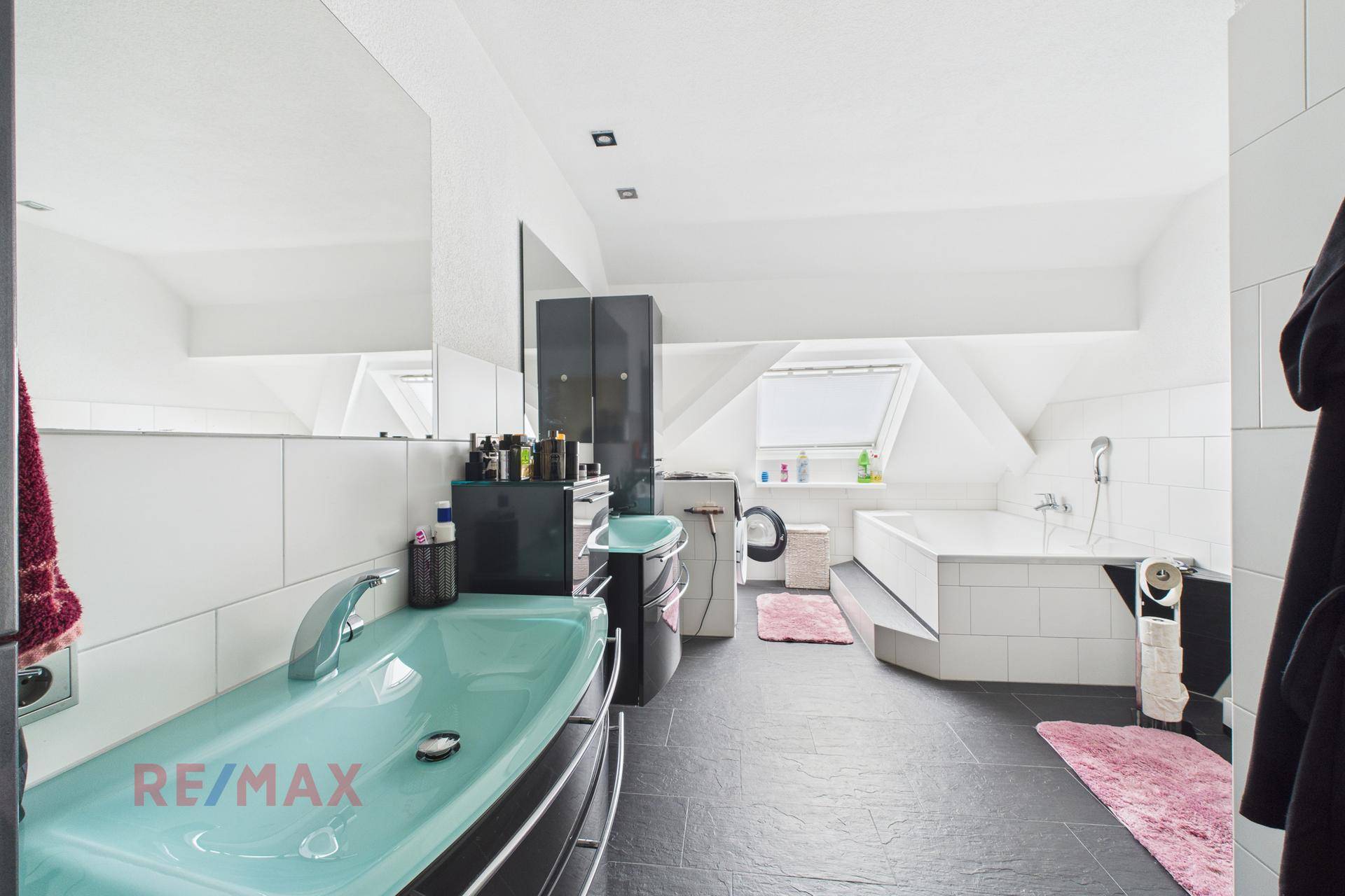 Helles Badezimmer im Dachgeschoss mit Badewanne, grünem Waschbecken und Dachfenster.