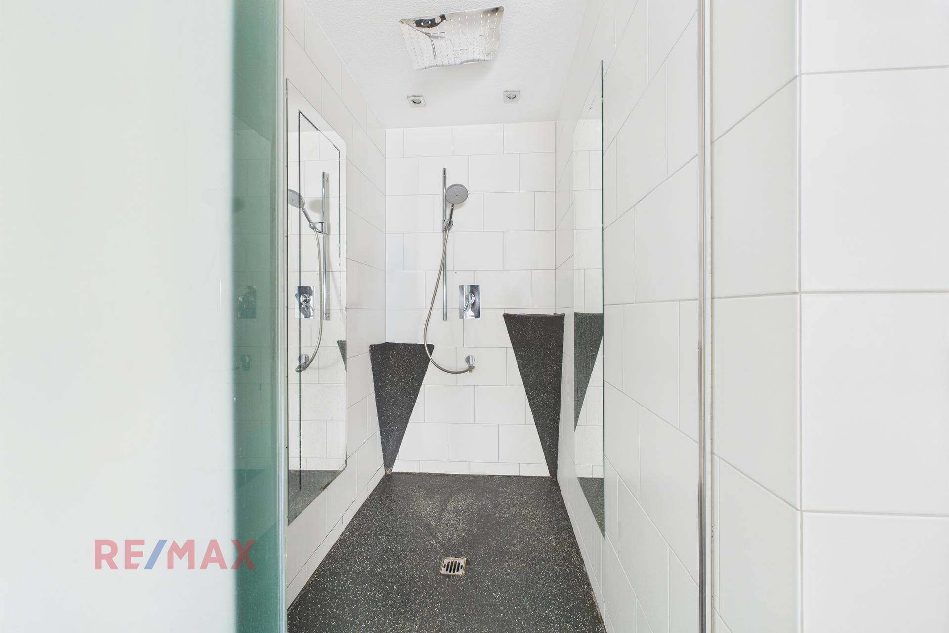 Moderne Duschkabine mit dunklem Boden und weißen Wandfliesen.