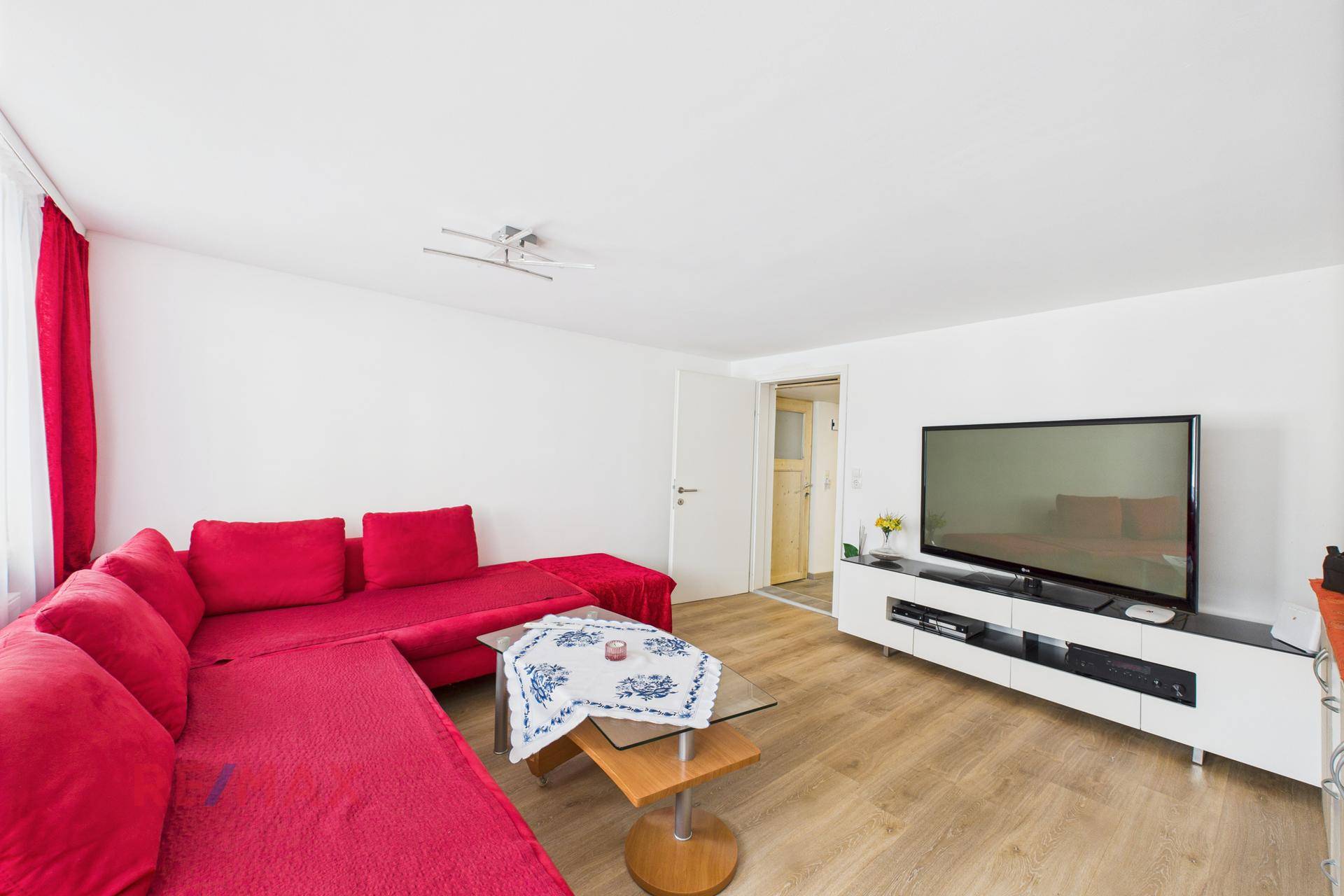 Wohnzimmer mit rotem Ecksofa, TV-Möbel und hellem Laminatboden.