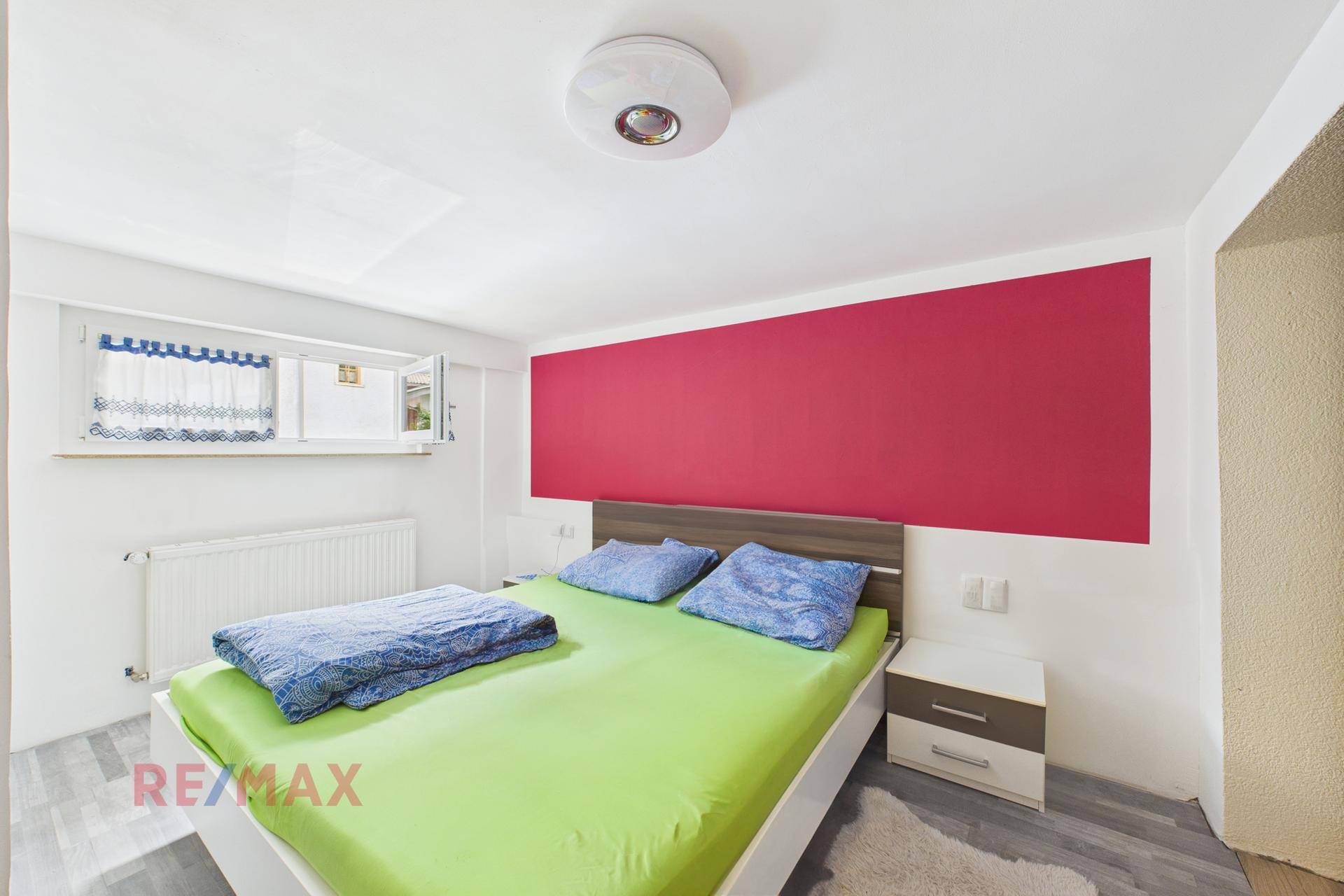 Schlafzimmer mit Doppelbett, farbiger Wand und hellem Laminatboden.