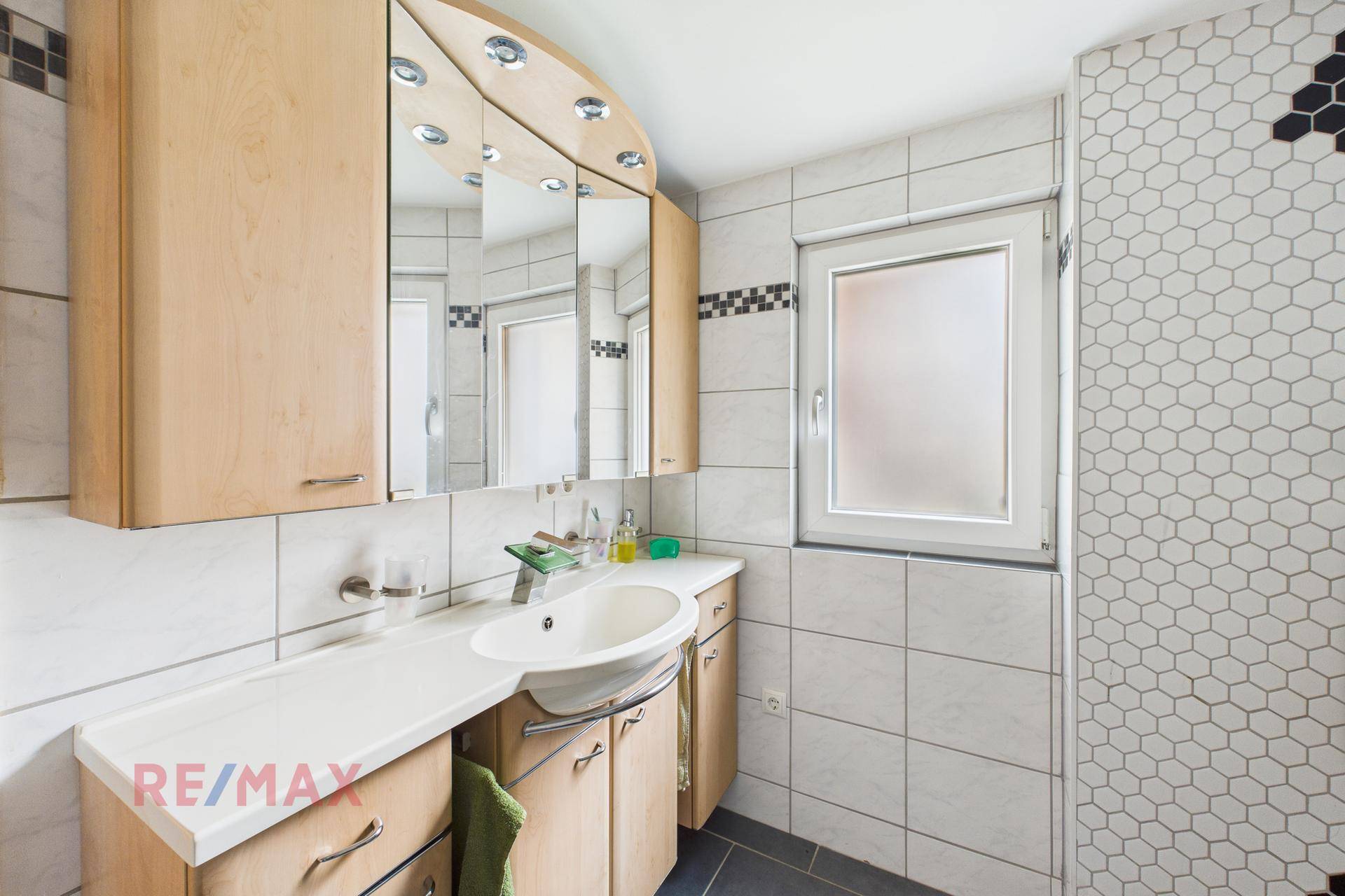 Badezimmer mit Waschtisch, Spiegelschrank und Fenster für Tageslicht.