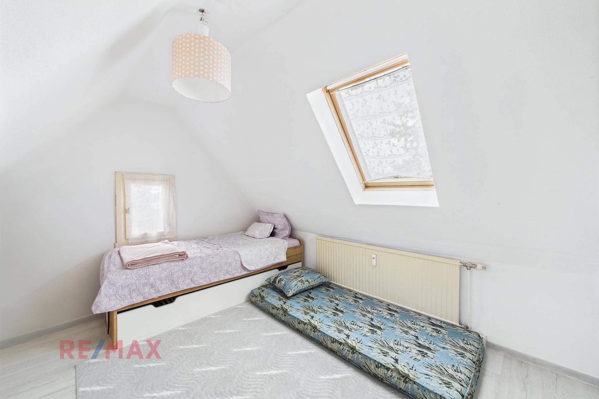 Helles Schlafzimmer unter Dachschräge mit Einzelbett, Dachfenster und Heizkörper.