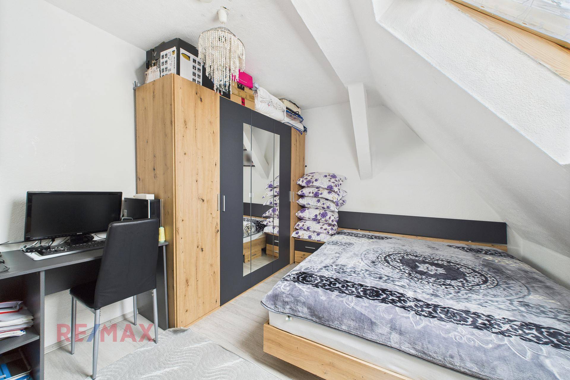 Schlafzimmer unter Dachschräge mit Bett, Schreibtisch und Kleiderschrank.