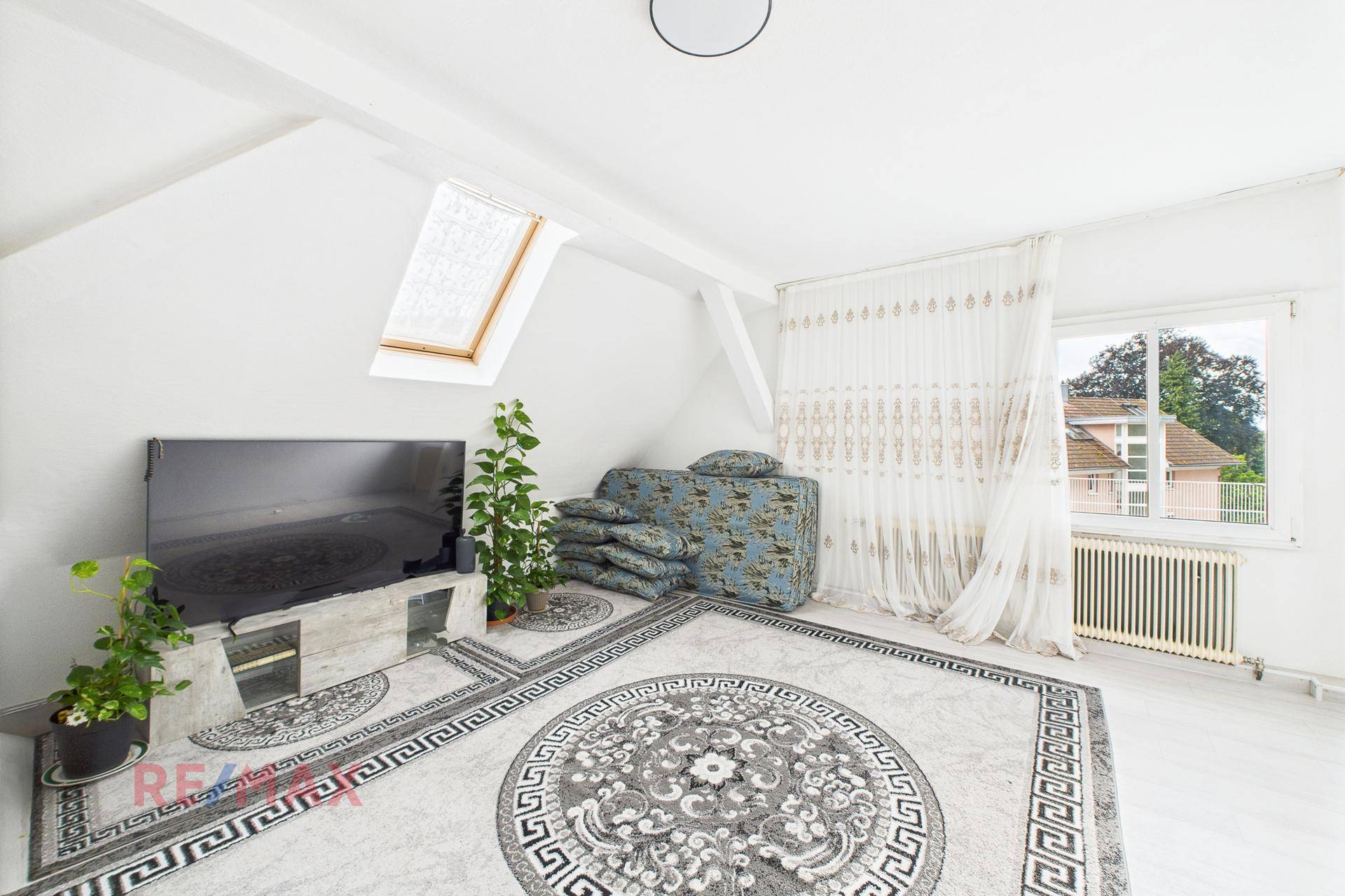 Gemütliches Wohnzimmer unter Dachschräge mit großem Teppich und Fernseher.