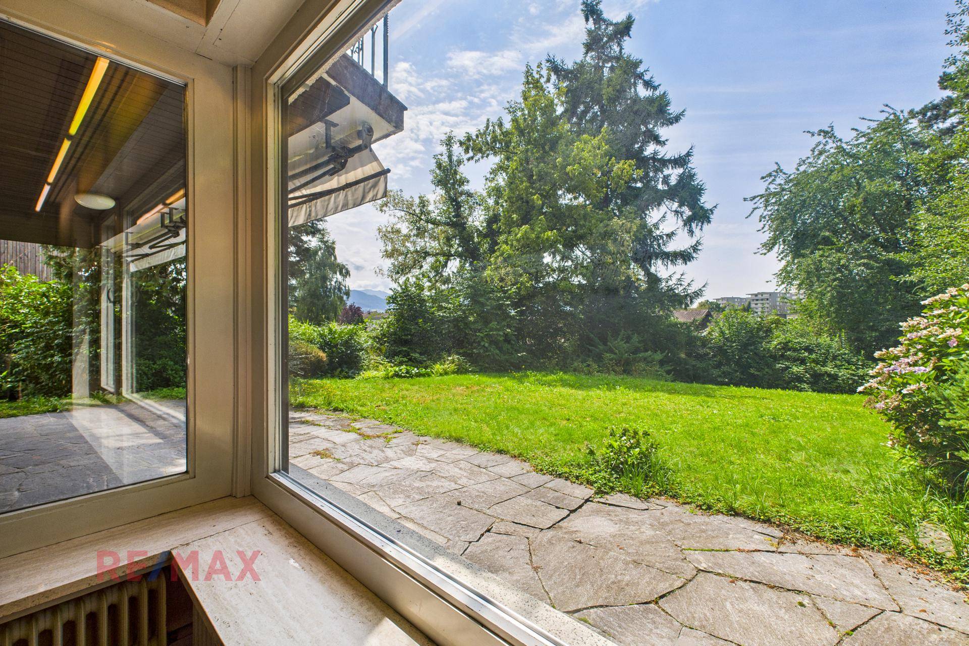 Blick vom Innenraum auf die gepflasterte Terrasse und den grünen Gartenbereich.