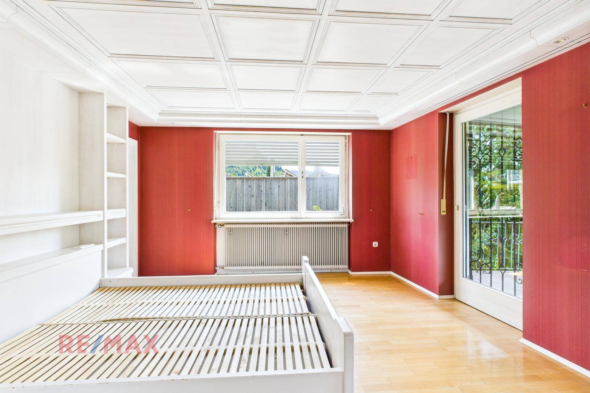 Schlafzimmer mit roter Wandgestaltung, Parkettboden und französischem Balkon.