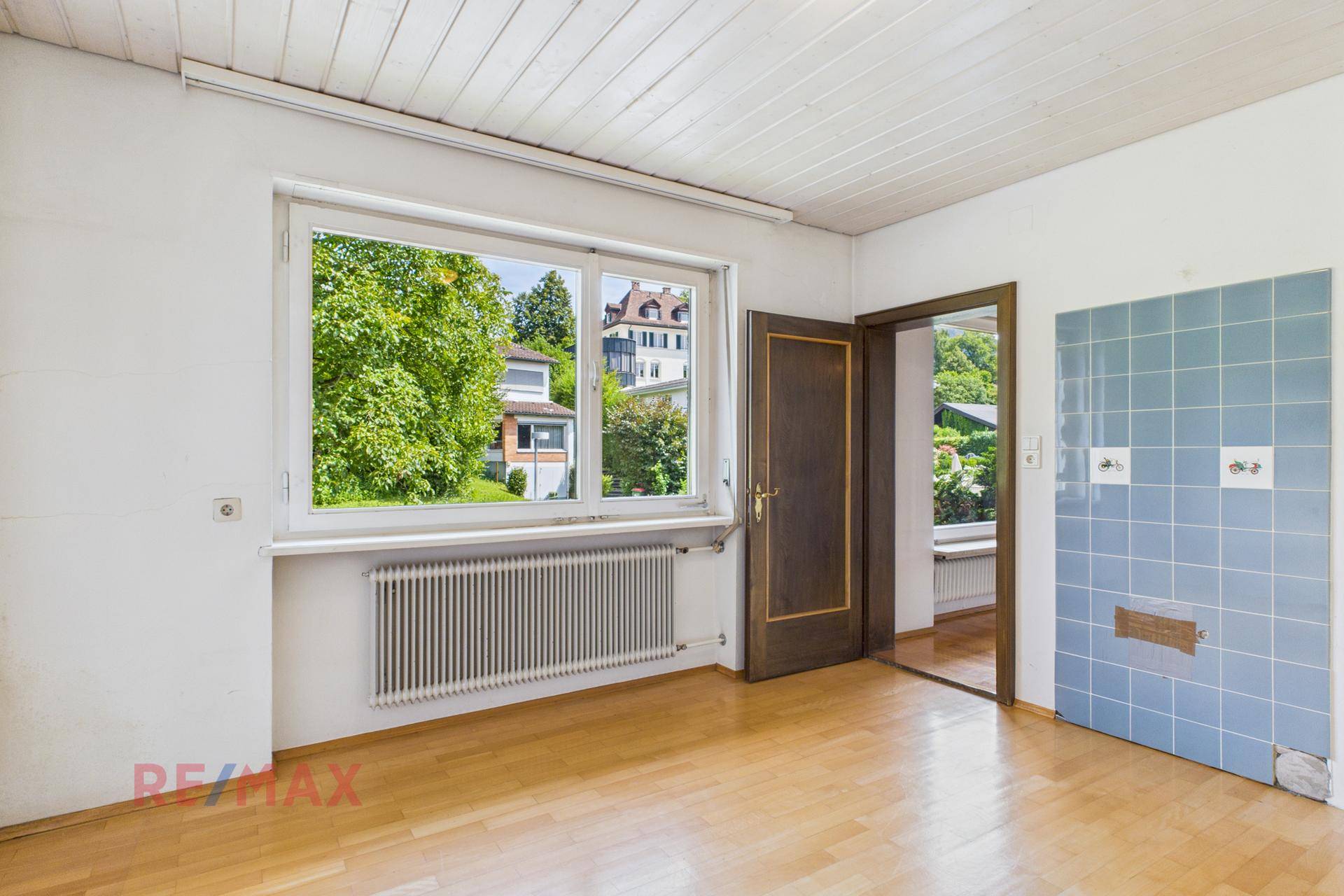 Zimmer mit Parkettboden, Fenster und blauer Wandfliesenverkleidung.