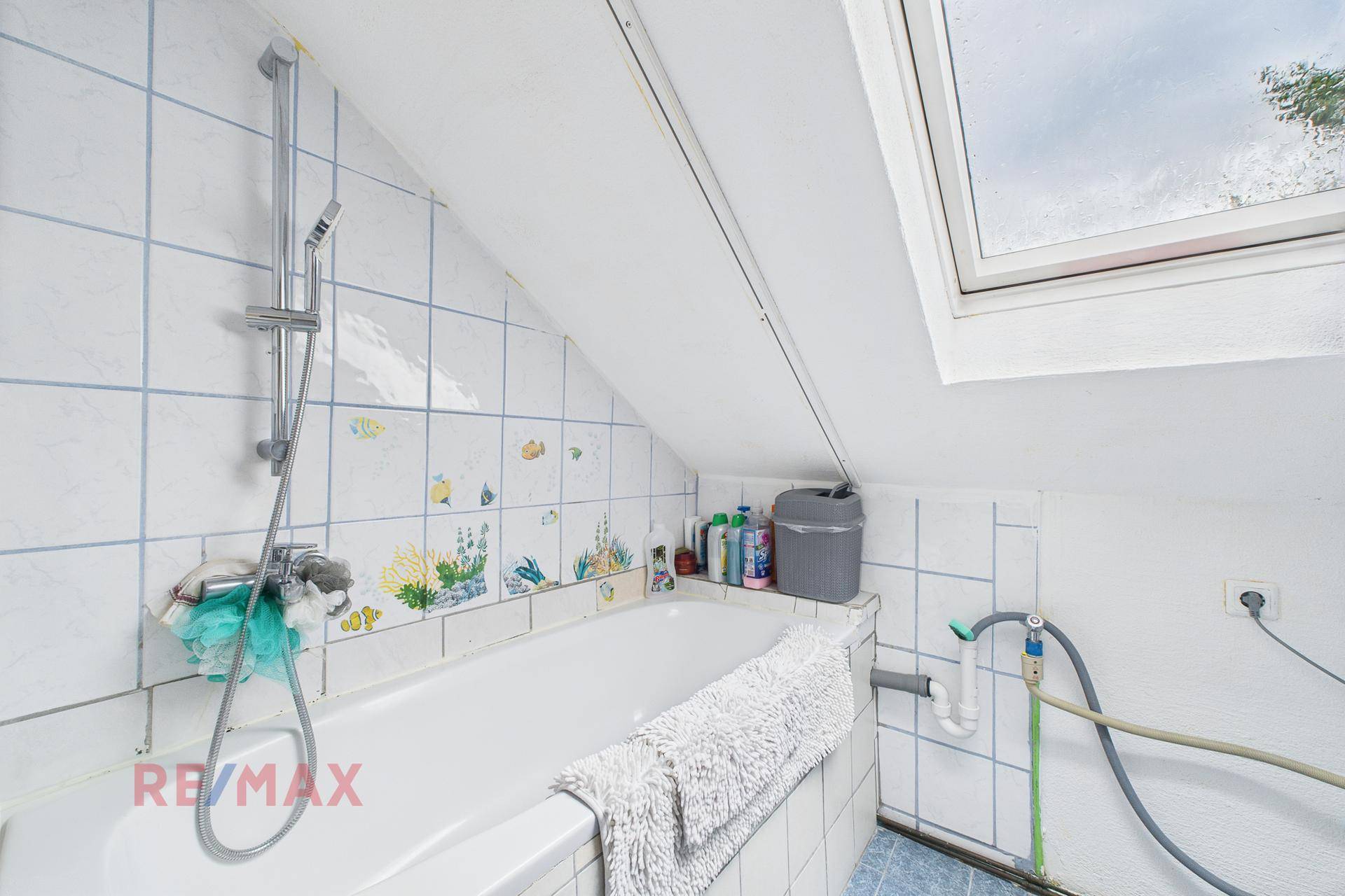 Badezimmer unter Dachschräge mit Badewanne, Fliesen und Dachfenster.