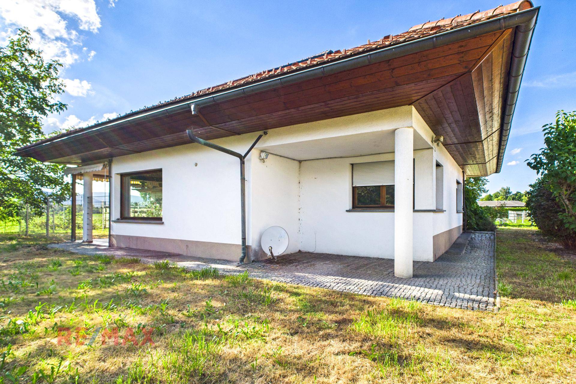 Seitenansicht des Hauses mit Rasenfläche und einem überdachten Bereich, der als Terrasse dienen könnte.