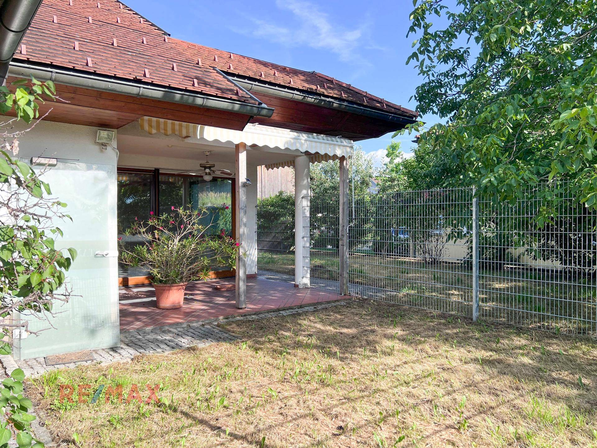 Überdachte Terrasse mit Topfpflanzen und Blick in den Garten, ideal für entspannte Stunden im Freien.