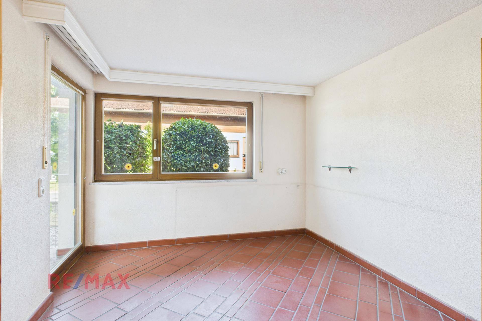 Leeres Zimmer mit Terrakottafliesen und großem Fenster, das viel Tageslicht hereinlässt.