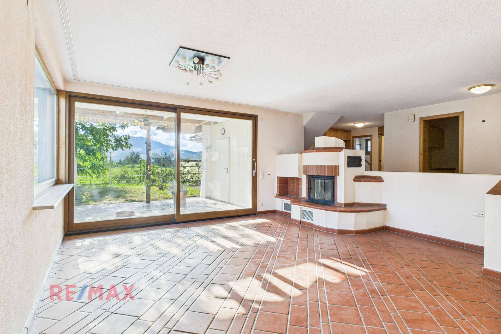 Geräumiges Wohnzimmer mit Kamin, großen Schiebetüren und Blick ins Grüne.