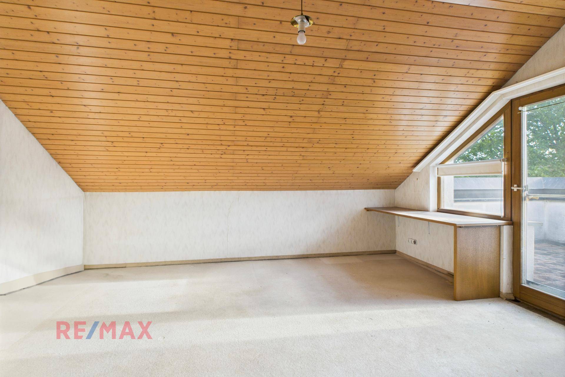 Helles Dachzimmer mit Holzdecke, Teppichboden und Zugang zur Terrasse.