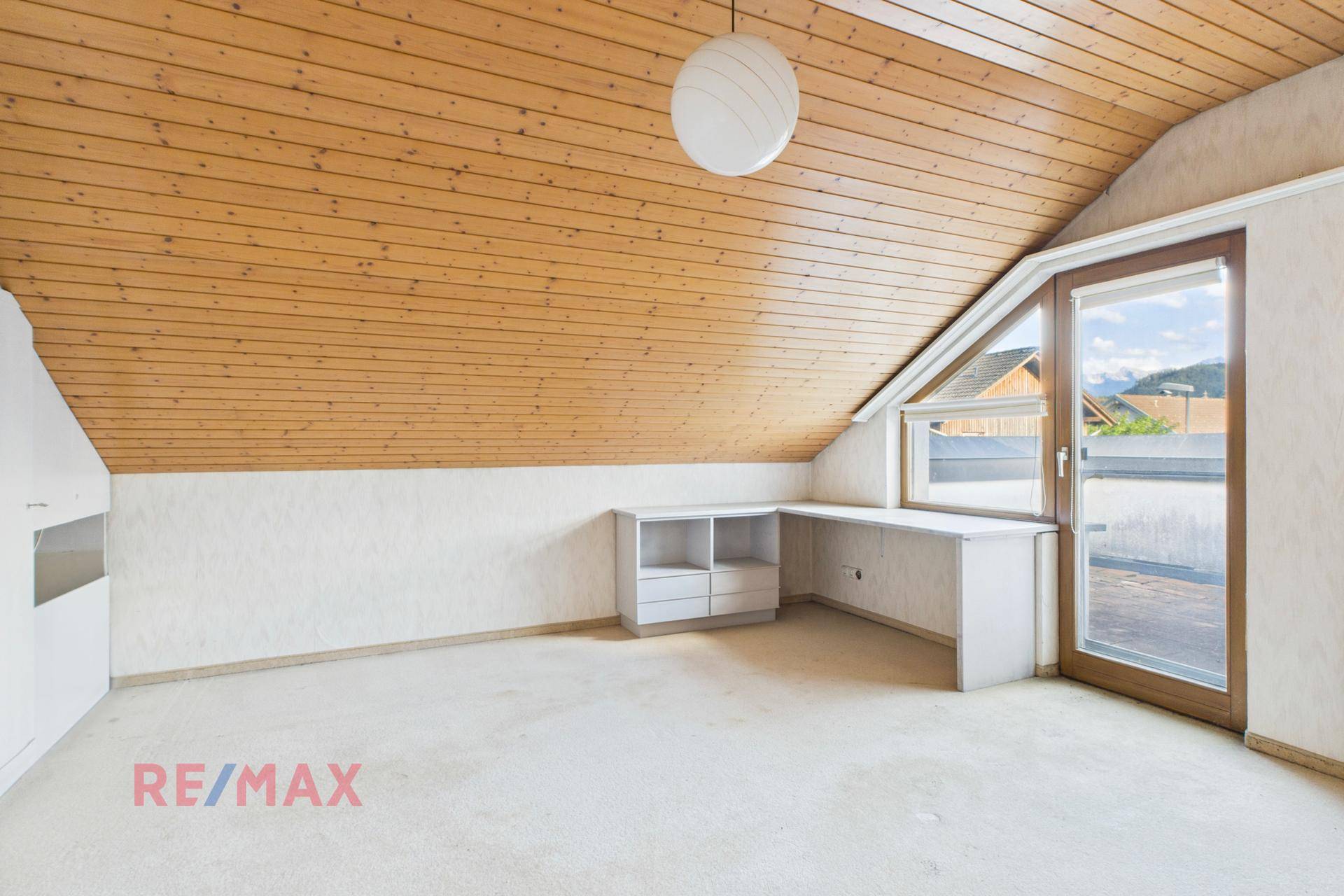 Dachzimmer mit Holzdecke, Teppichboden und integriertem Schreibtisch, ideal als Arbeits- oder Schlafzimmer.