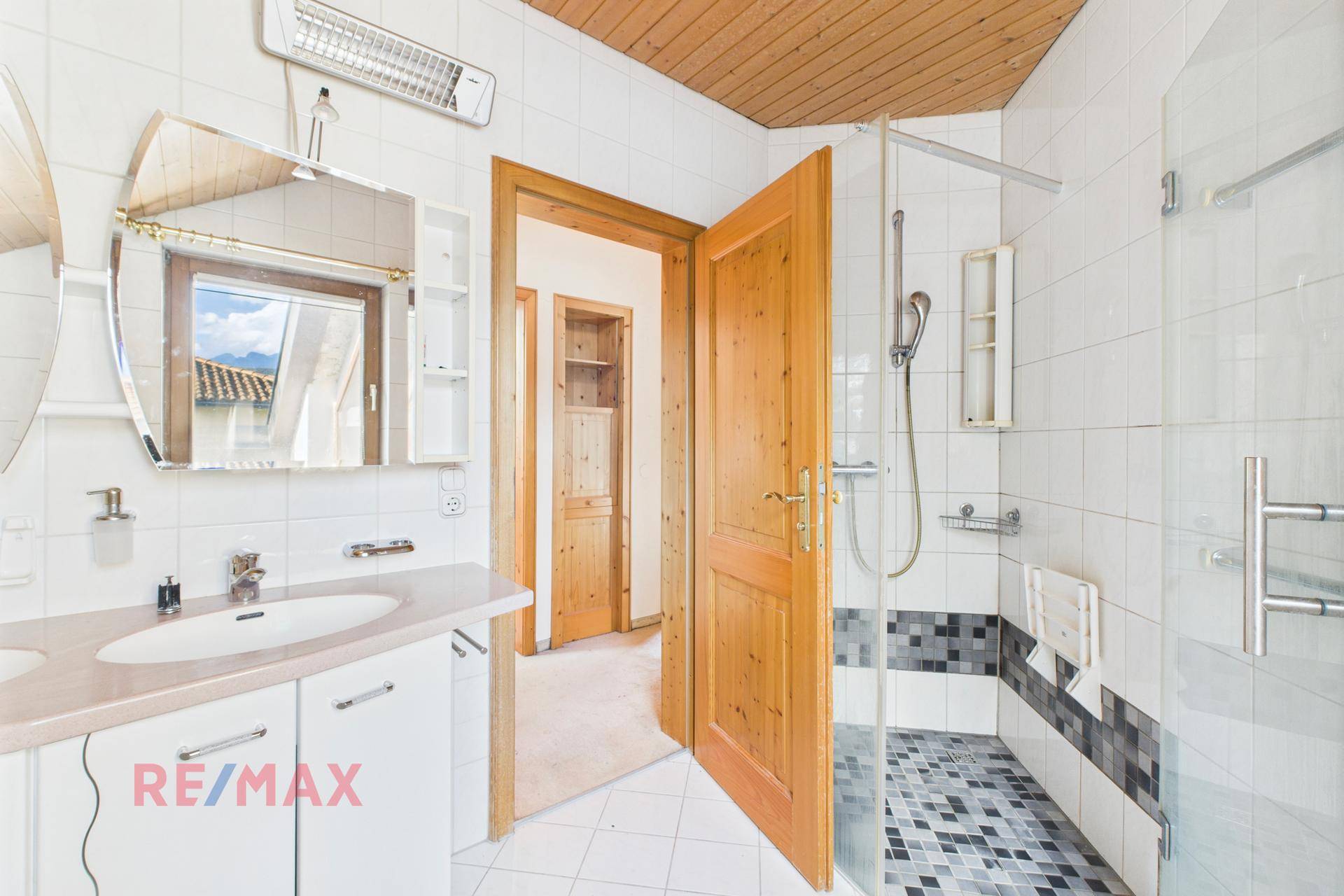 Badezimmer mit Dusche, Waschbecken und Holzdecke, modern gefliest.