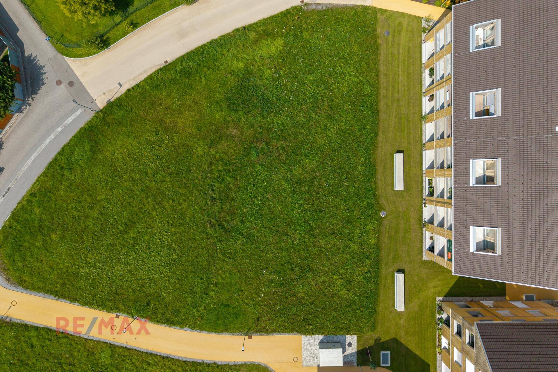 Senkrechte Luftaufnahme des grünen Baugrundstücks mit angrenzenden Wegen und modernen Gebäuden.