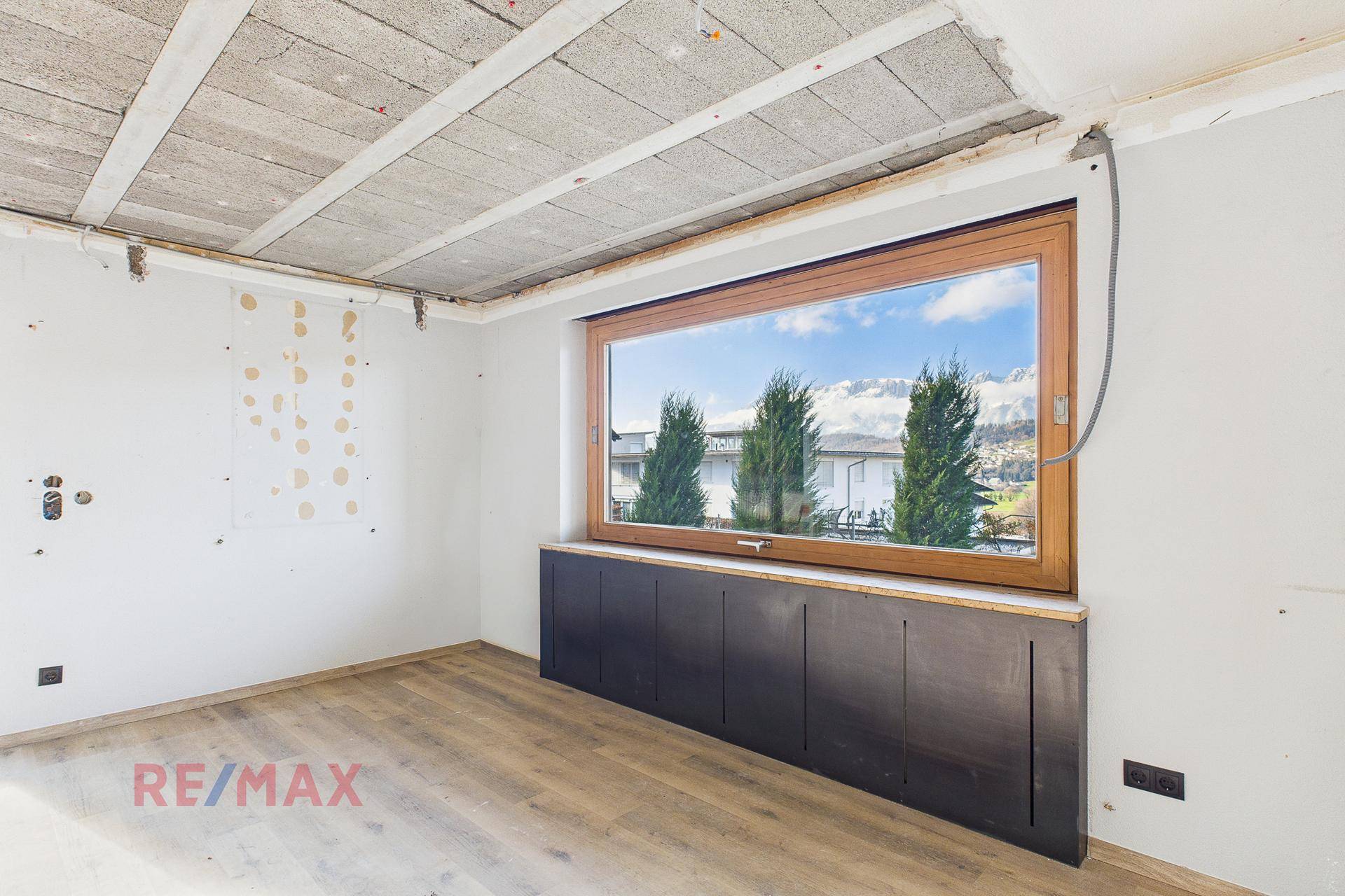 Heller Raum im Rohbau mit großem Fenster und Blick auf die umliegende Landschaft.
