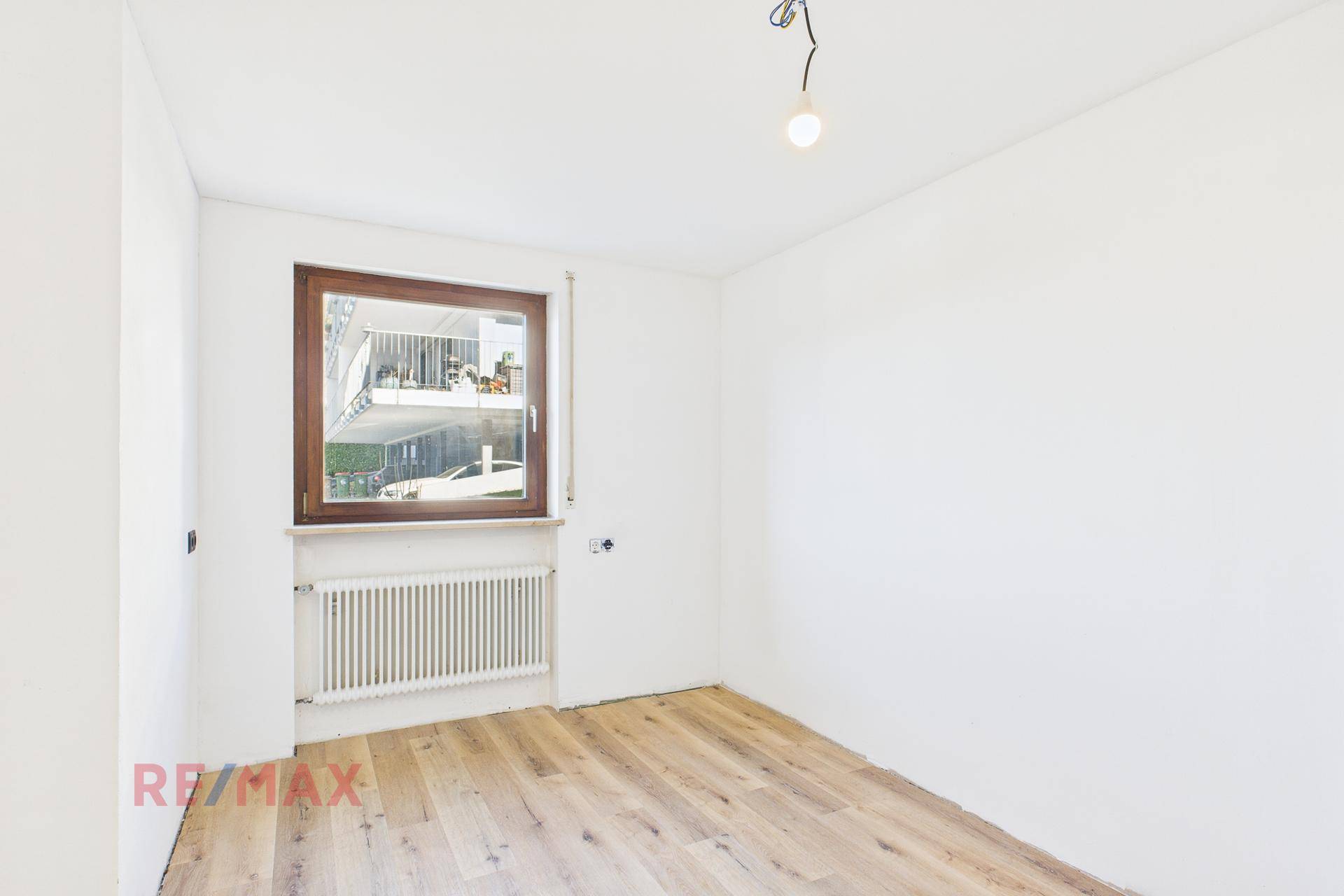 Schlafzimmer mit Parkettboden und Fenster, das einen Blick auf den Nachbarbalkon bietet.