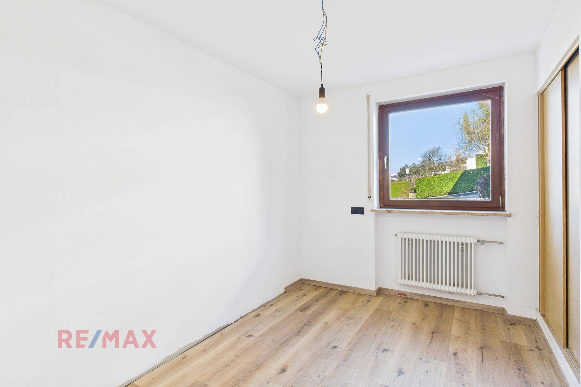 Helles Schlafzimmer mit Parkettboden und Fenster zum grünen Außenbereich.