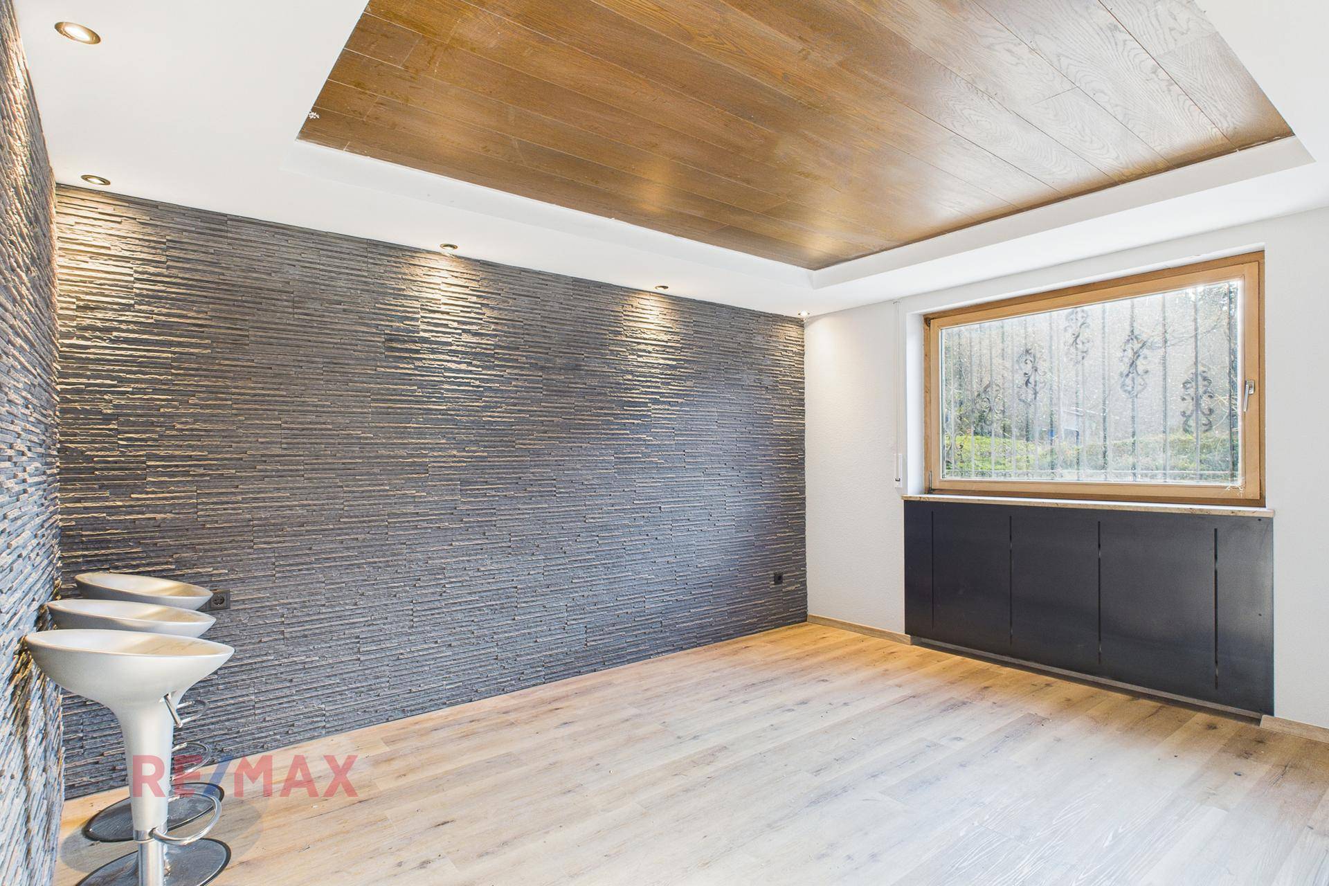 Modern gestalteter Raum mit Steinwand, Holzdecke und Fenster zum Gartenbereich.