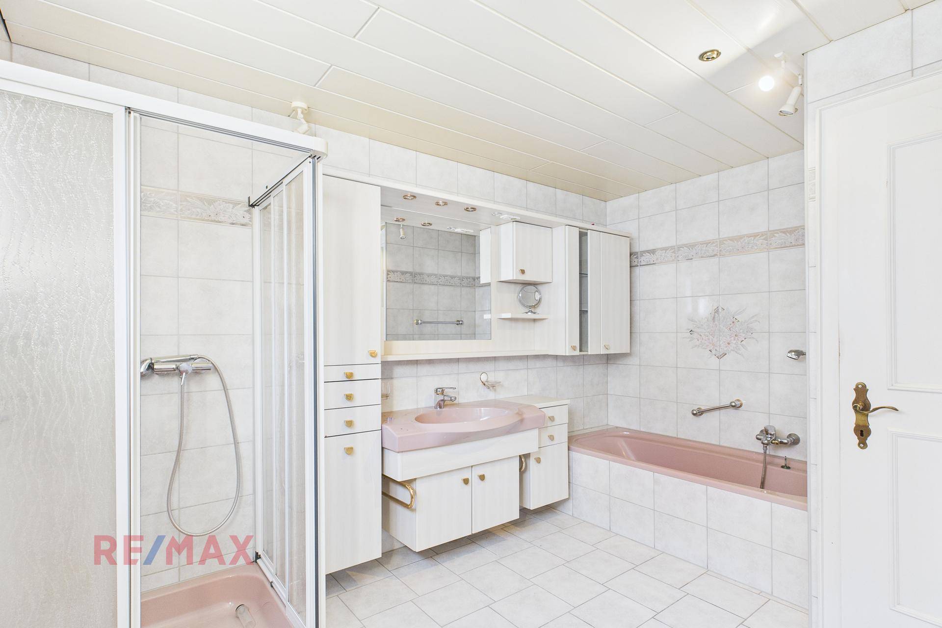 Badezimmer im 80er-Jahre-Stil mit Badewanne, Dusche und rosa Waschbecken.