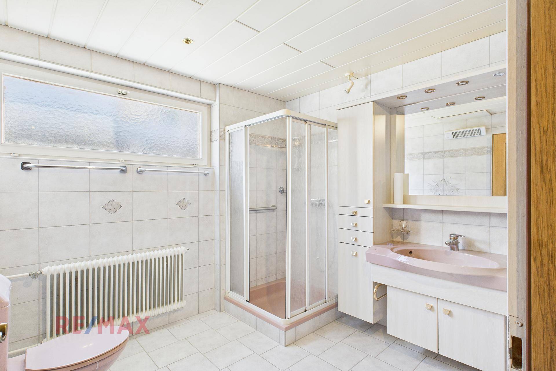 Badezimmer im 80er-Jahre-Stil mit Dusche, rosa Waschbecken und Fenster.
