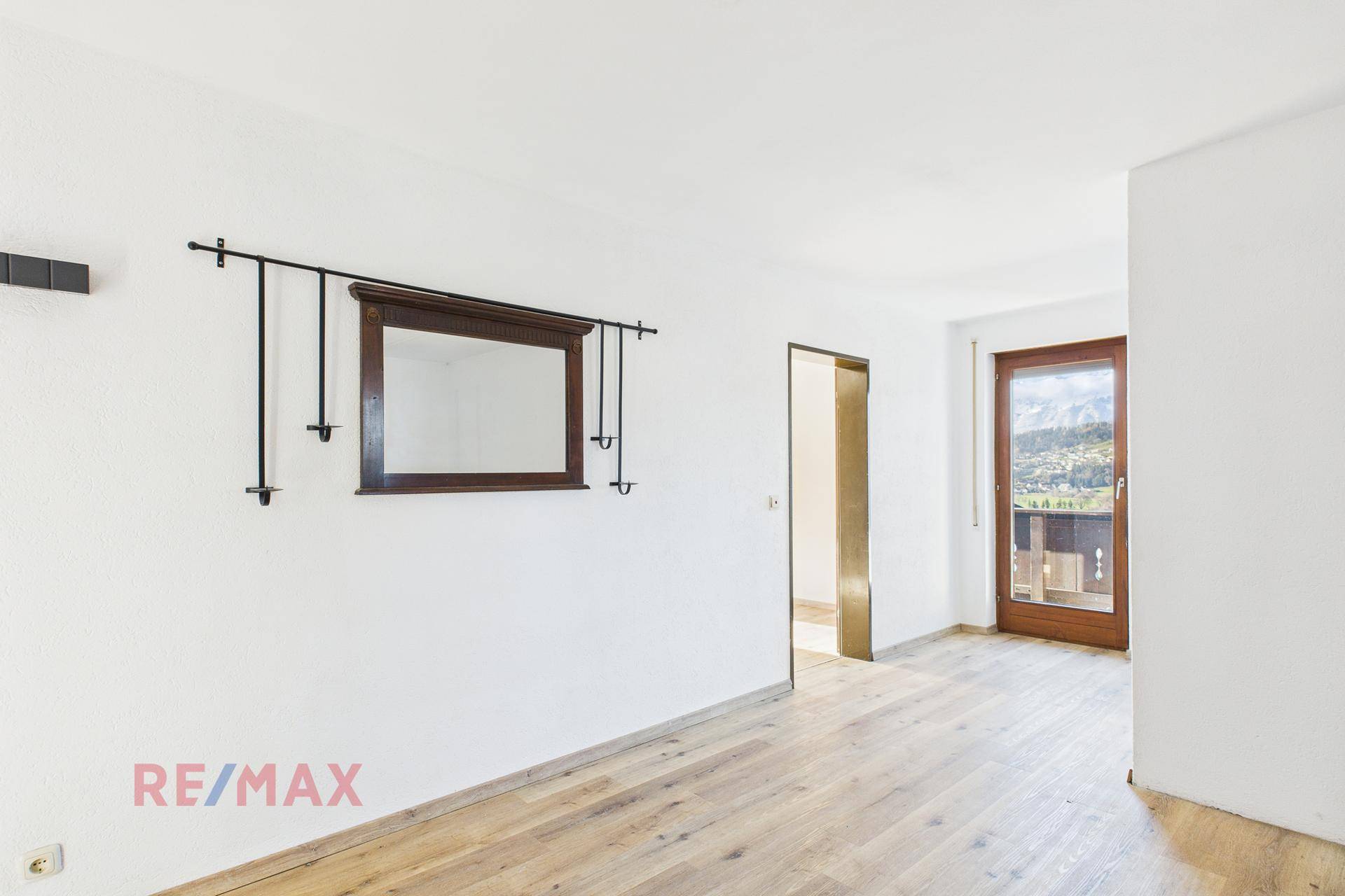 Heller Raum mit Parkettboden, dekorativem Spiegel und Zugang zu einem Balkon.