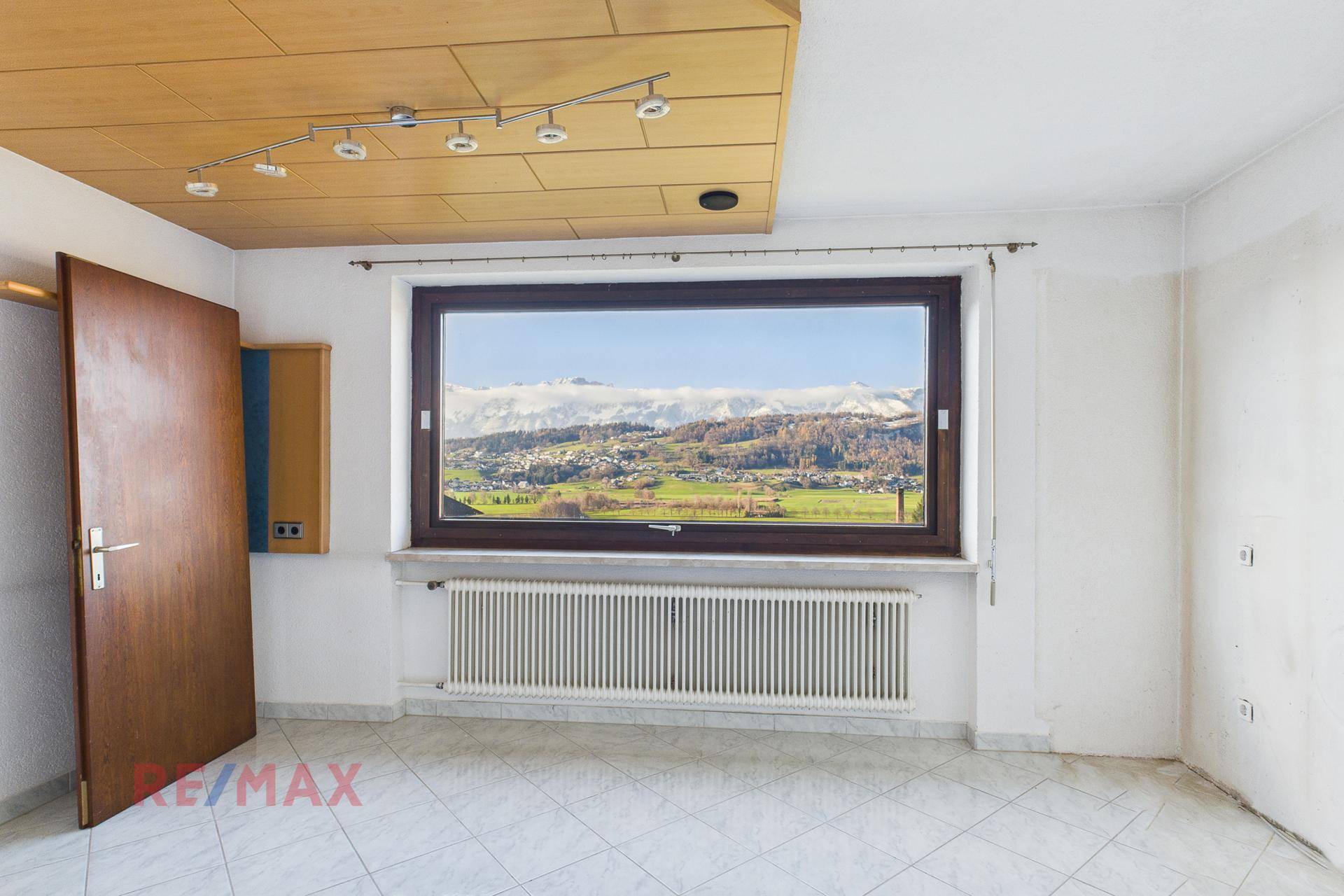 Geräumiges Zimmer mit Fliesenboden, Holzdecke und weitem Bergblick.