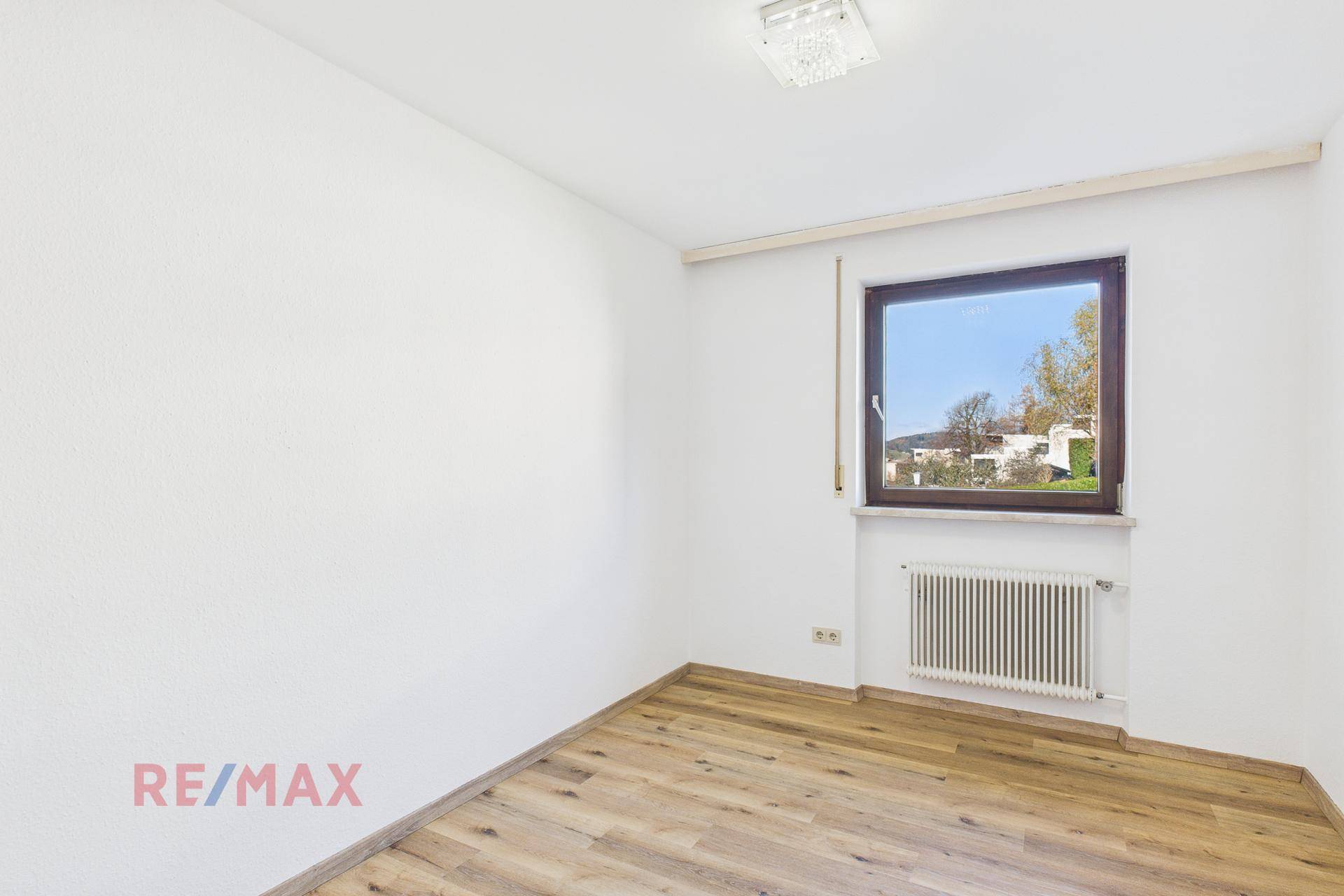 Helles Schlafzimmer mit Parkettboden und Fenster zum grünen Außenbereich.