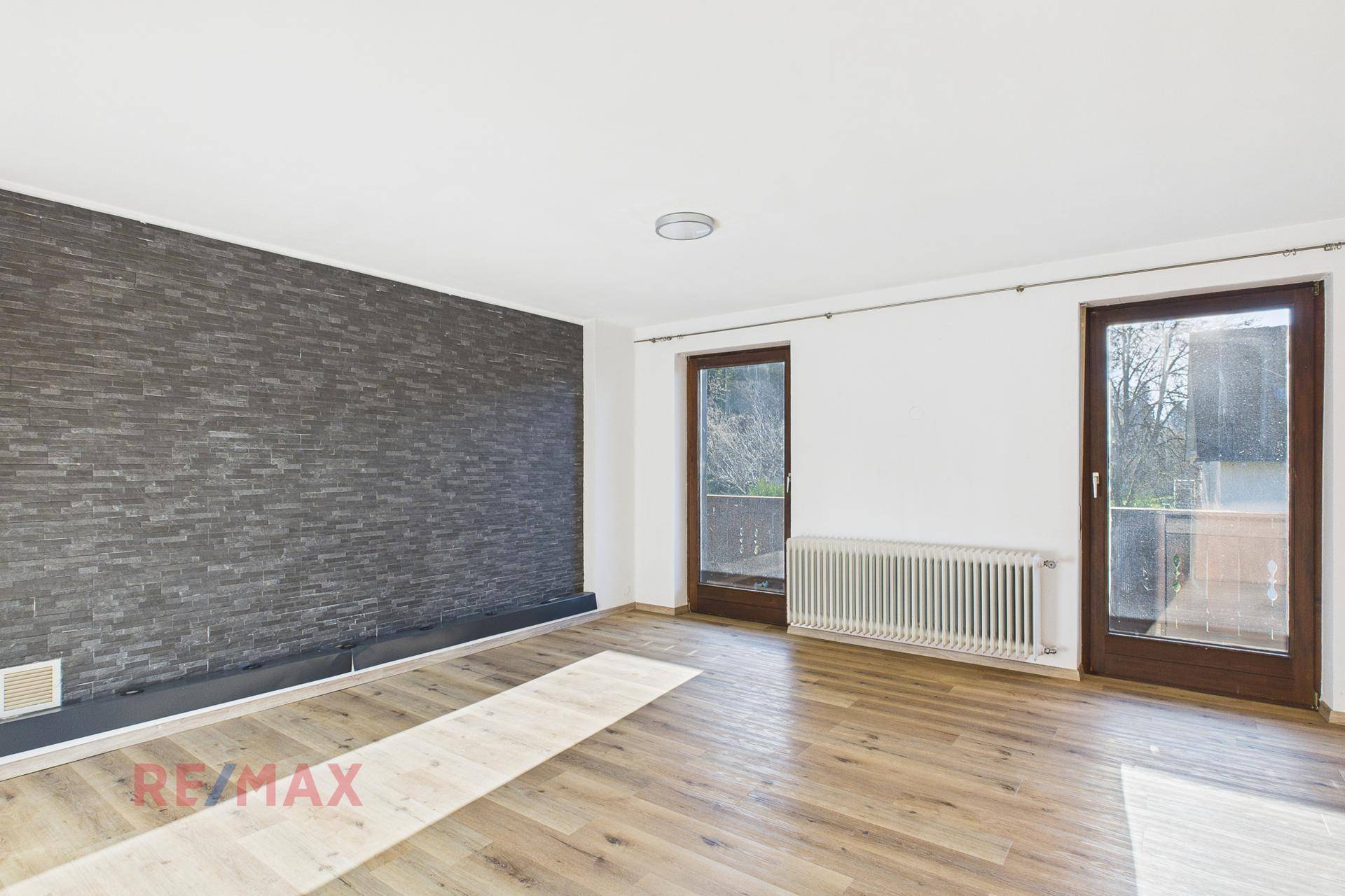 Wohnzimmer mit Steinwandverkleidung, Parkettboden und Zugang zu zwei Balkonen.