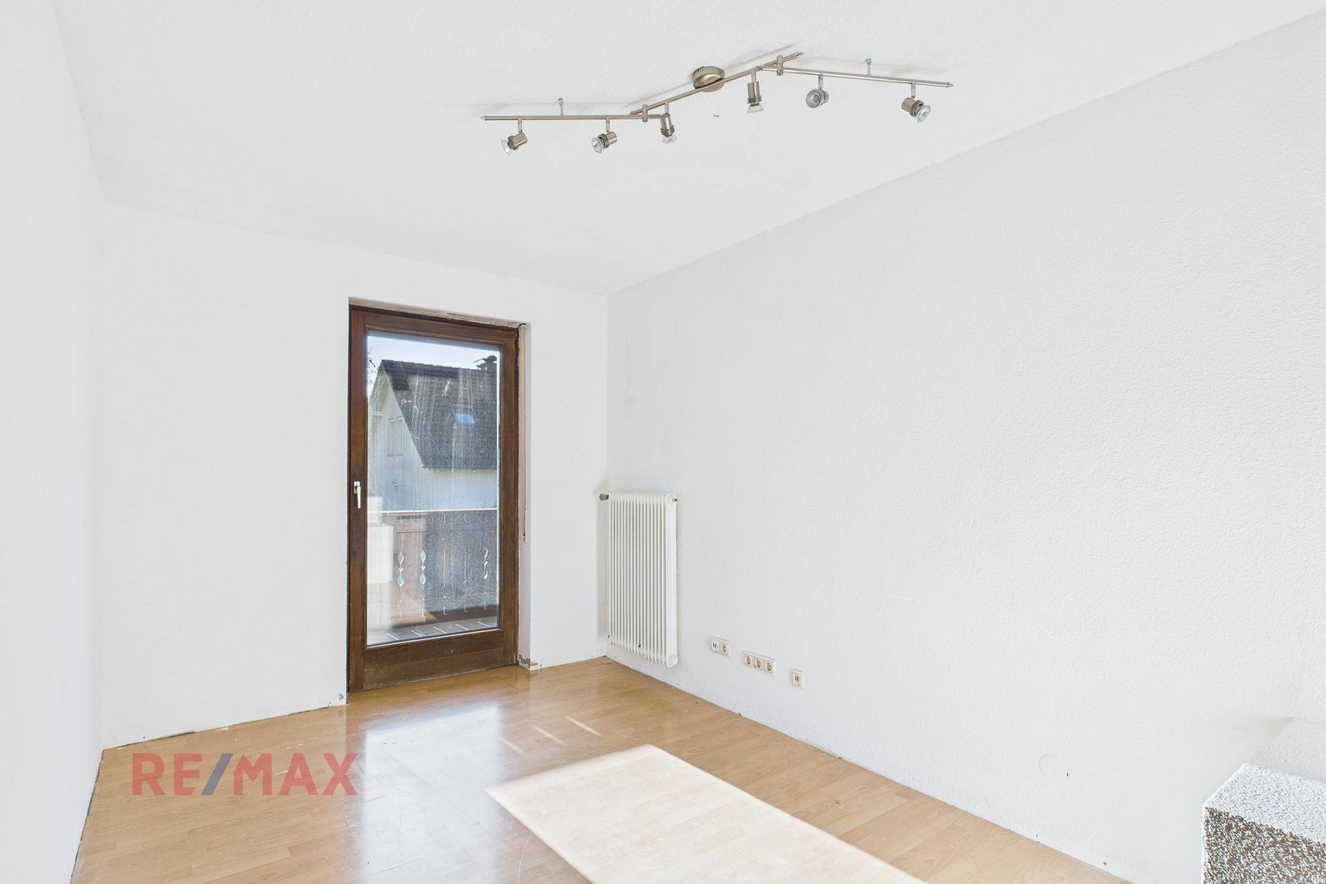 Schlafzimmer mit Parkettboden und Fenstertür, die auf einen Außenbereich führt.
