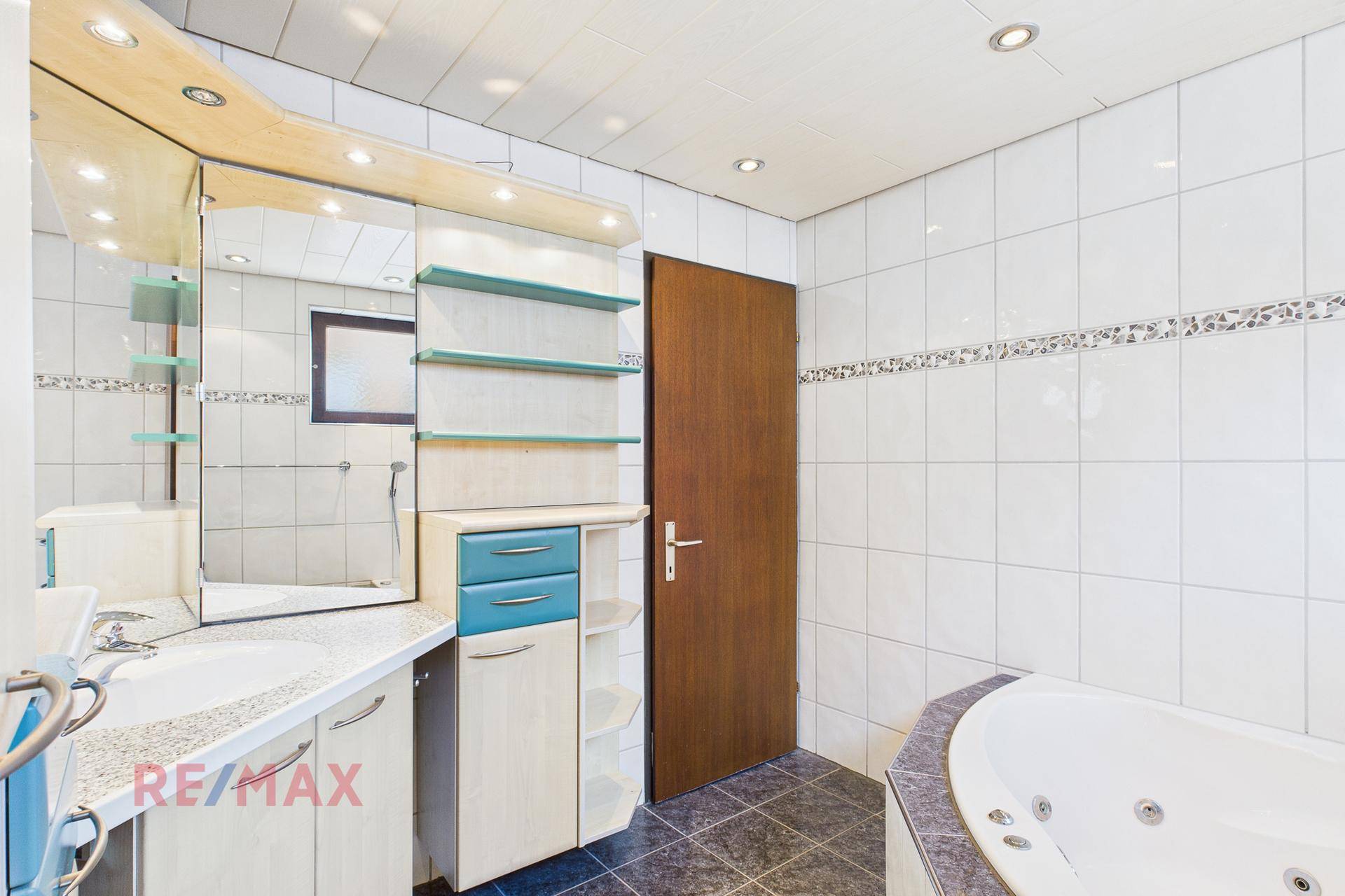 Geräumiges Badezimmer mit Whirlpool-Badewanne, Waschtisch und viel Stauraum.