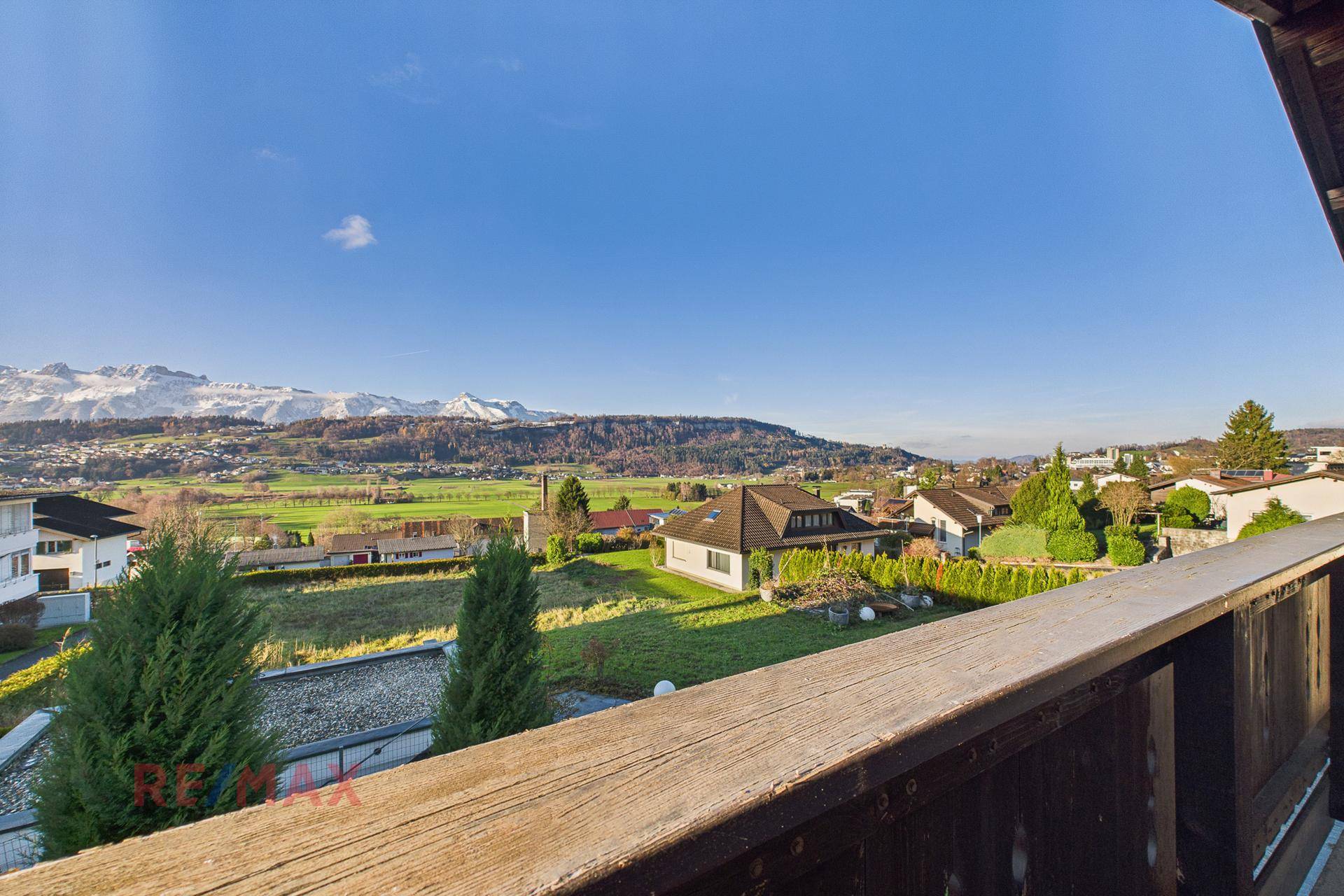Panoramablick vom Balkon auf die schneebedeckten Berge und das grüne Tal.