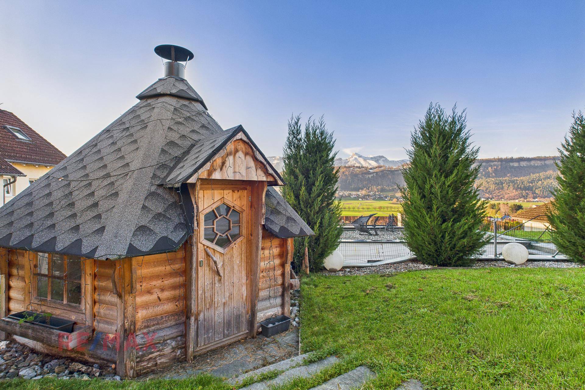 Gartenbereich mit rustikaler Holzhütte, Pool und weitem Bergblick.