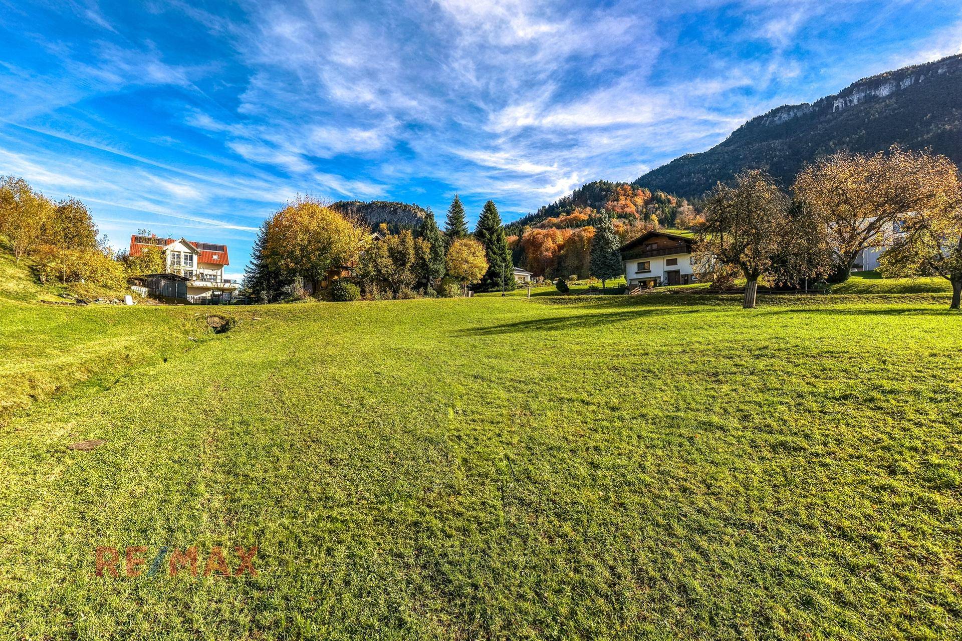 Idyllische grüne Wiese unter blauem Himmel mit Blick auf die herbstliche Berglandschaft.